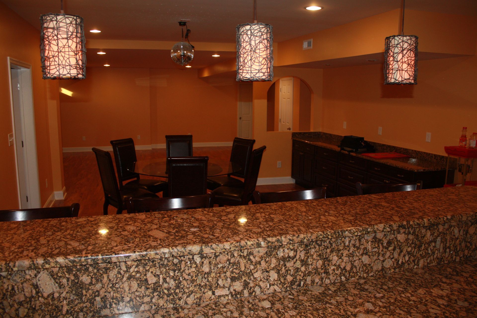 Bar area with granite countertop and seating; orange walls, hanging lamps, and a round table.