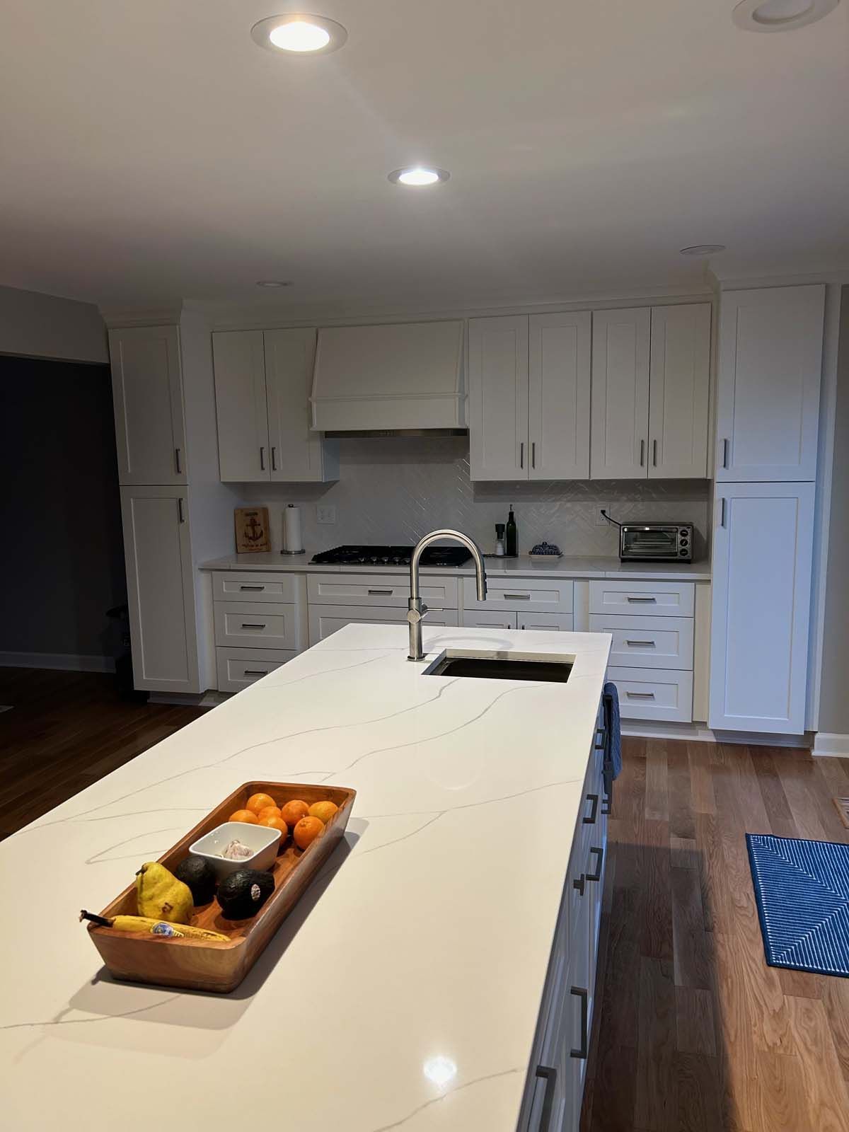 White kitchen with island, cabinets, and countertops. Fruit tray on the island.