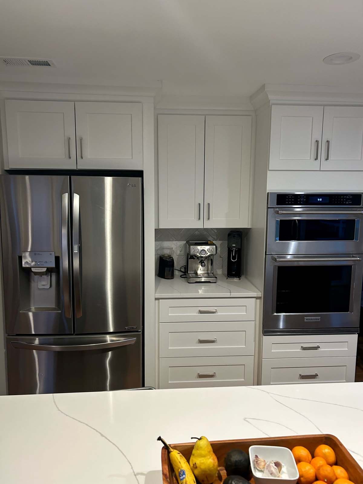Stainless steel fridge, built-in microwave/oven combo, coffee station in white kitchen cabinets.