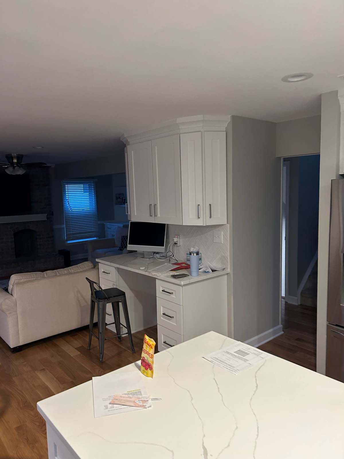 A kitchen with white cabinets, a built-in desk, and a stainless steel refrigerator.