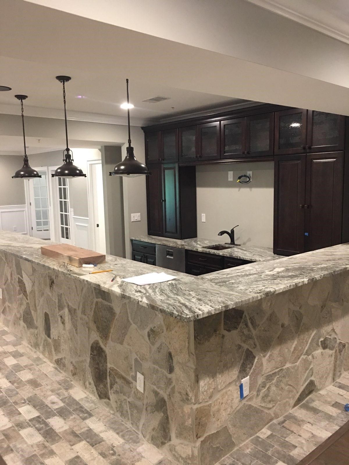 Kitchen with stone bar, dark cabinets, granite countertop, pendant lights, and gray walls.