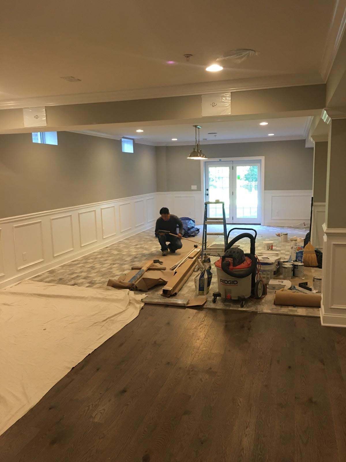A person kneels in a room under renovation; hardwood flooring and paneling is being installed.