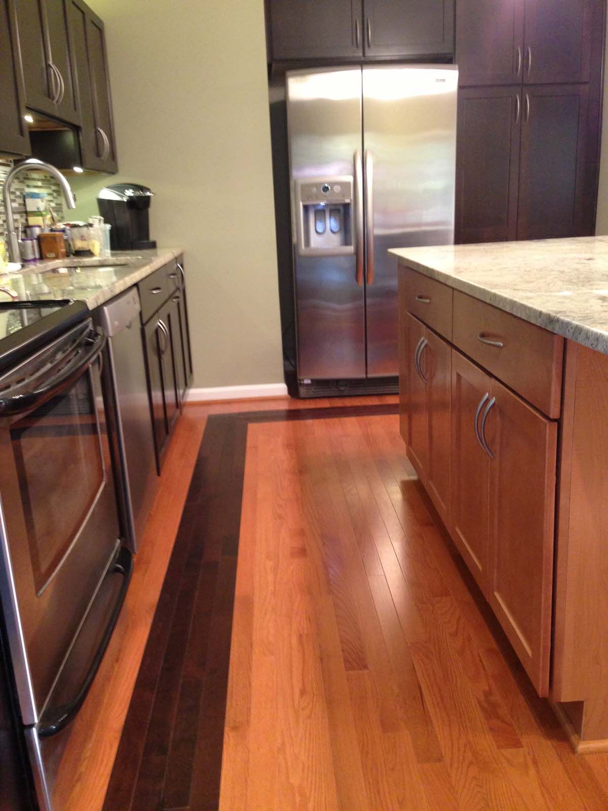Kitchen with stainless steel appliances, brown and light wood cabinets, and a contrasting dark wood floor border.