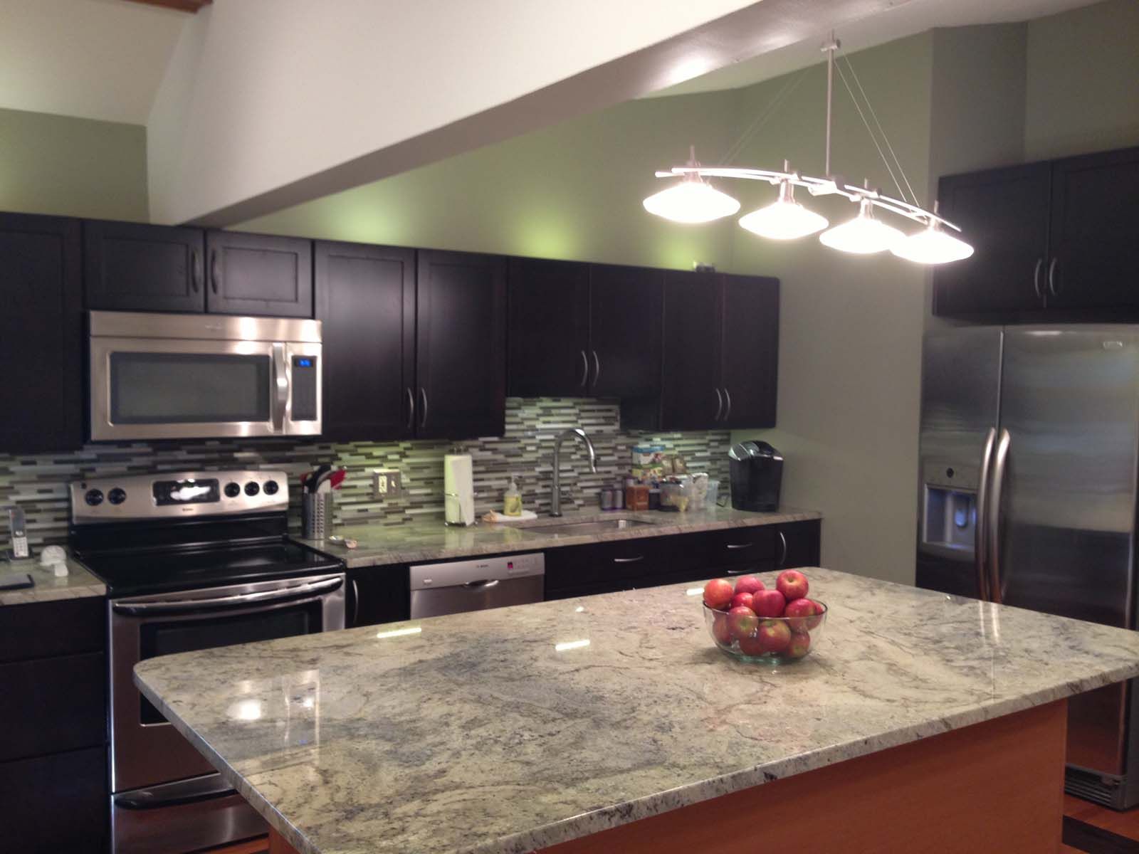 Modern kitchen with dark cabinets, stainless steel appliances, granite island, and green wall.