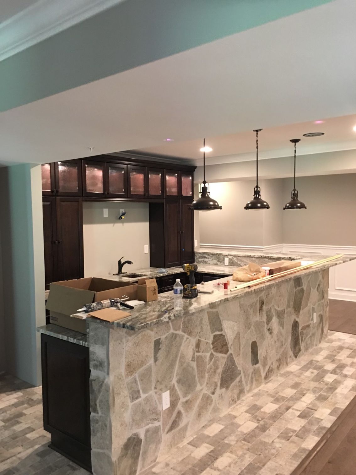 Basement bar with stone facade, dark wood cabinets, granite countertops, and pendant lights.