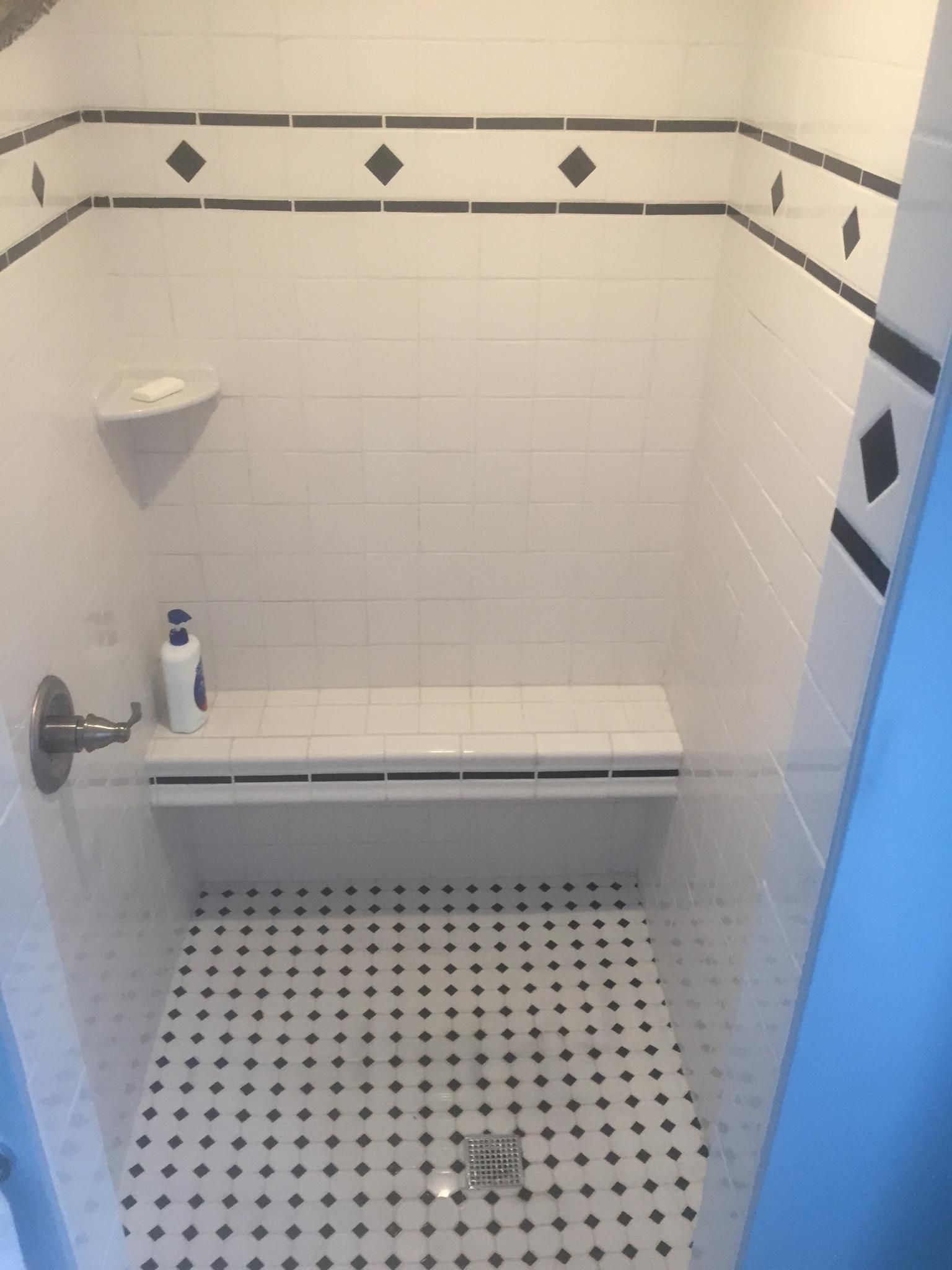 White tiled shower with black accents, built-in bench and small black and white floor tiles.