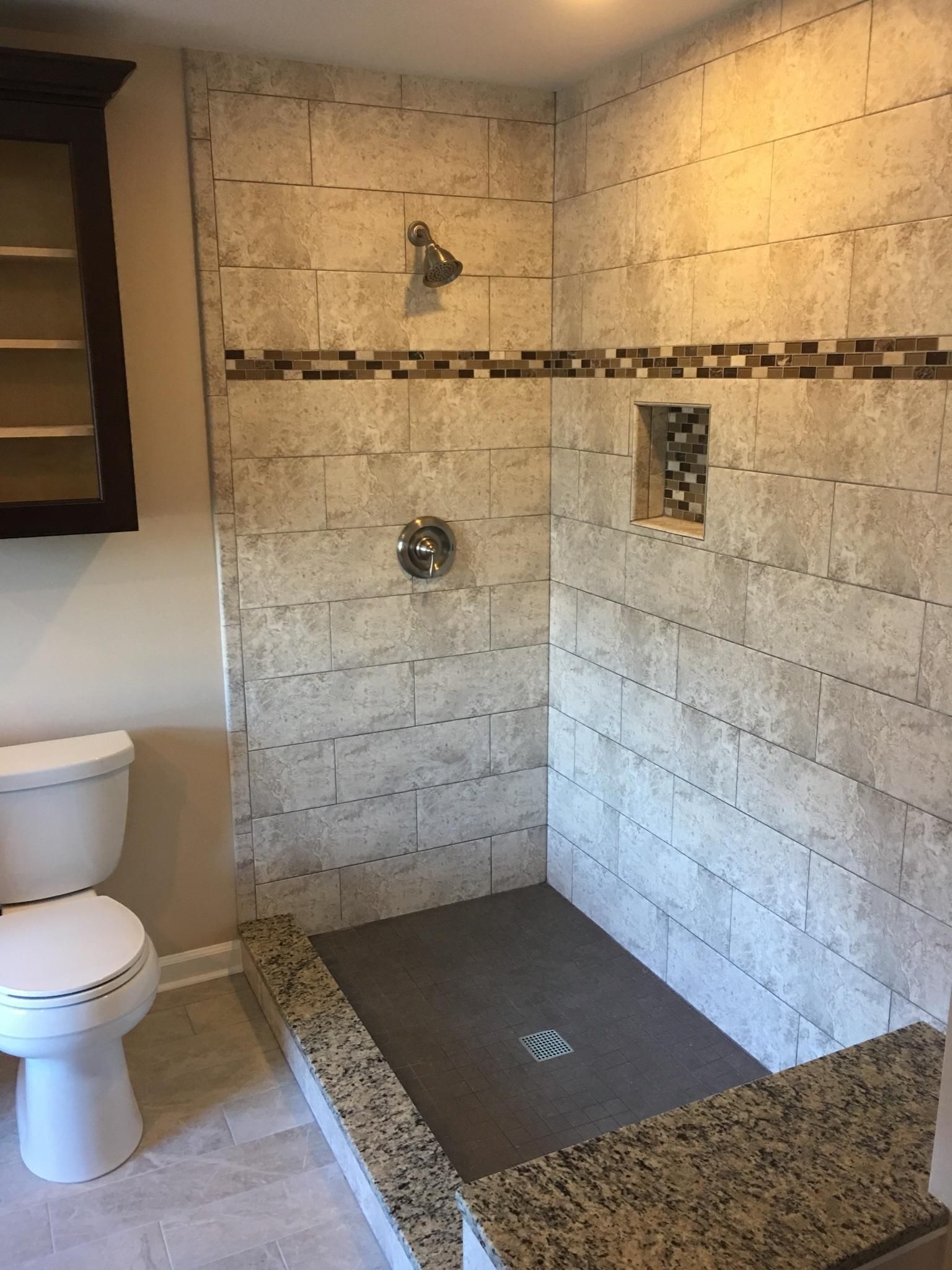 Bathroom with tile shower, toilet, and dark brown cabinet. The shower has a gray floor.