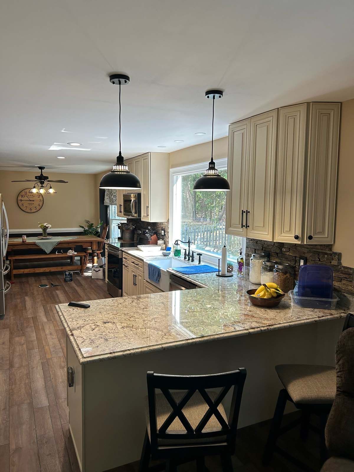 A modern kitchen with black pendant lights, a granite countertop, and a wooden dining table in the background.