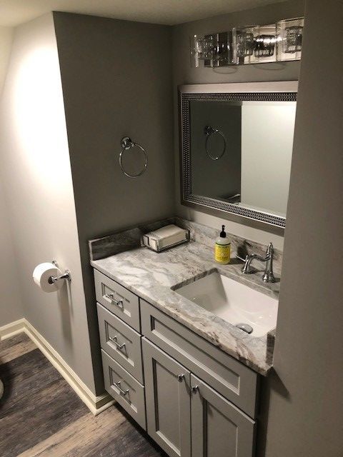 Small gray bathroom with vanity, mirror, and silver fixtures.