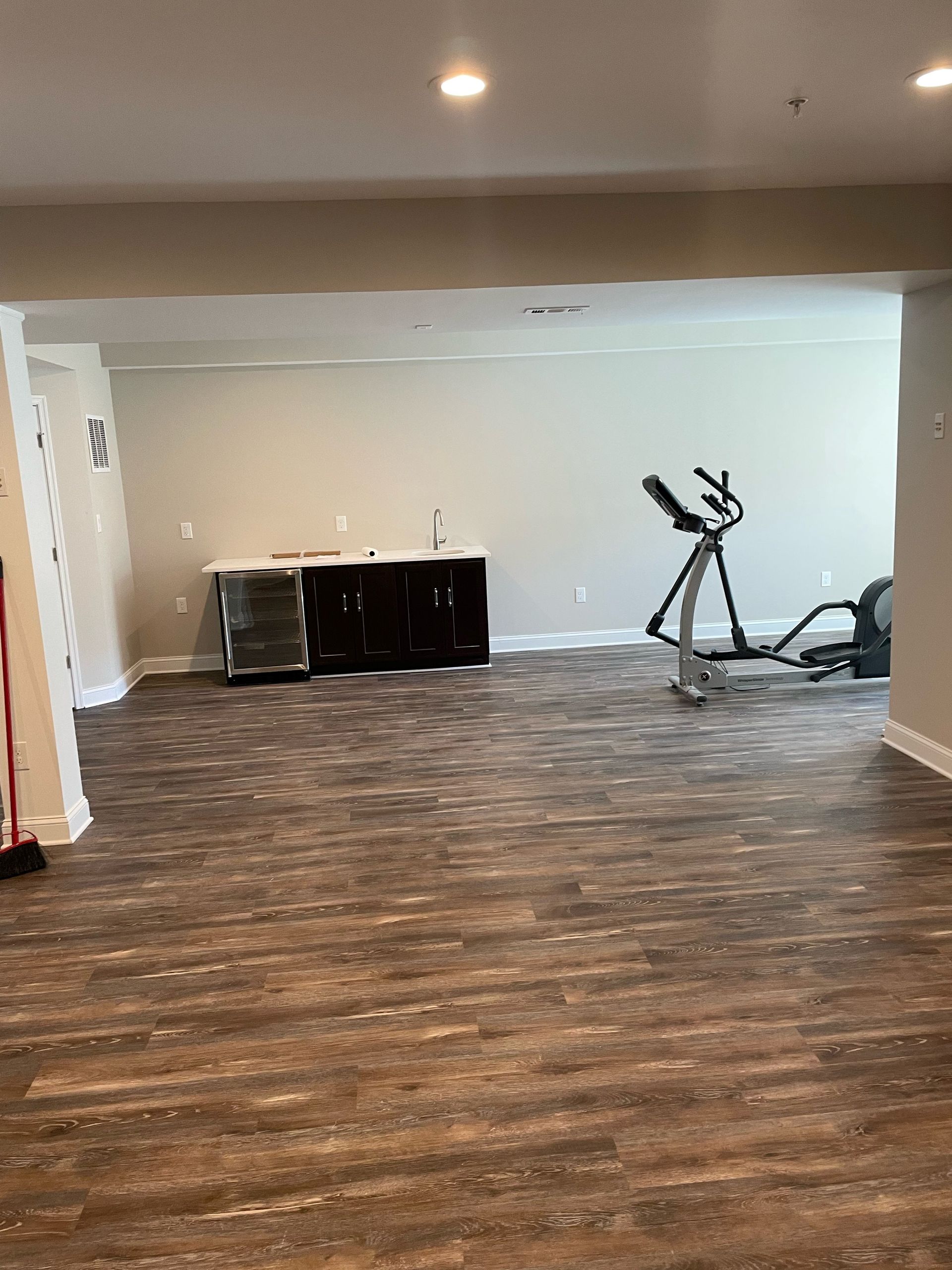 Empty room with wood-look flooring, exercise equipment, and a dark cabinet against the wall.