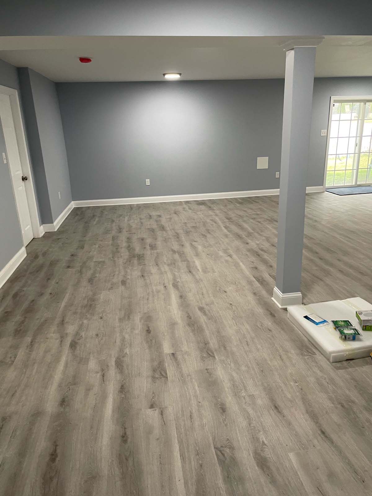 A spacious, freshly painted room with gray walls and wood-look flooring, pillar and door frame.