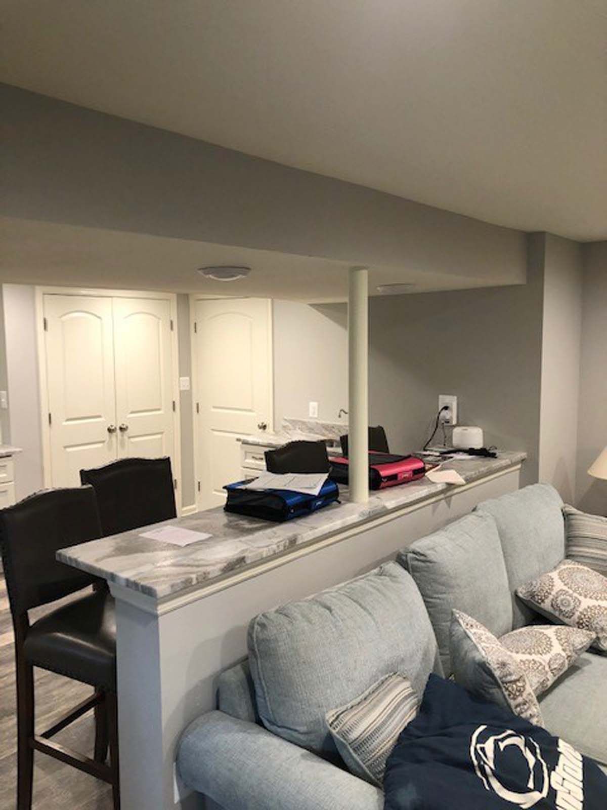 A finished basement with a bar, seating, and storage doors. Gray walls and a light blue sofa.