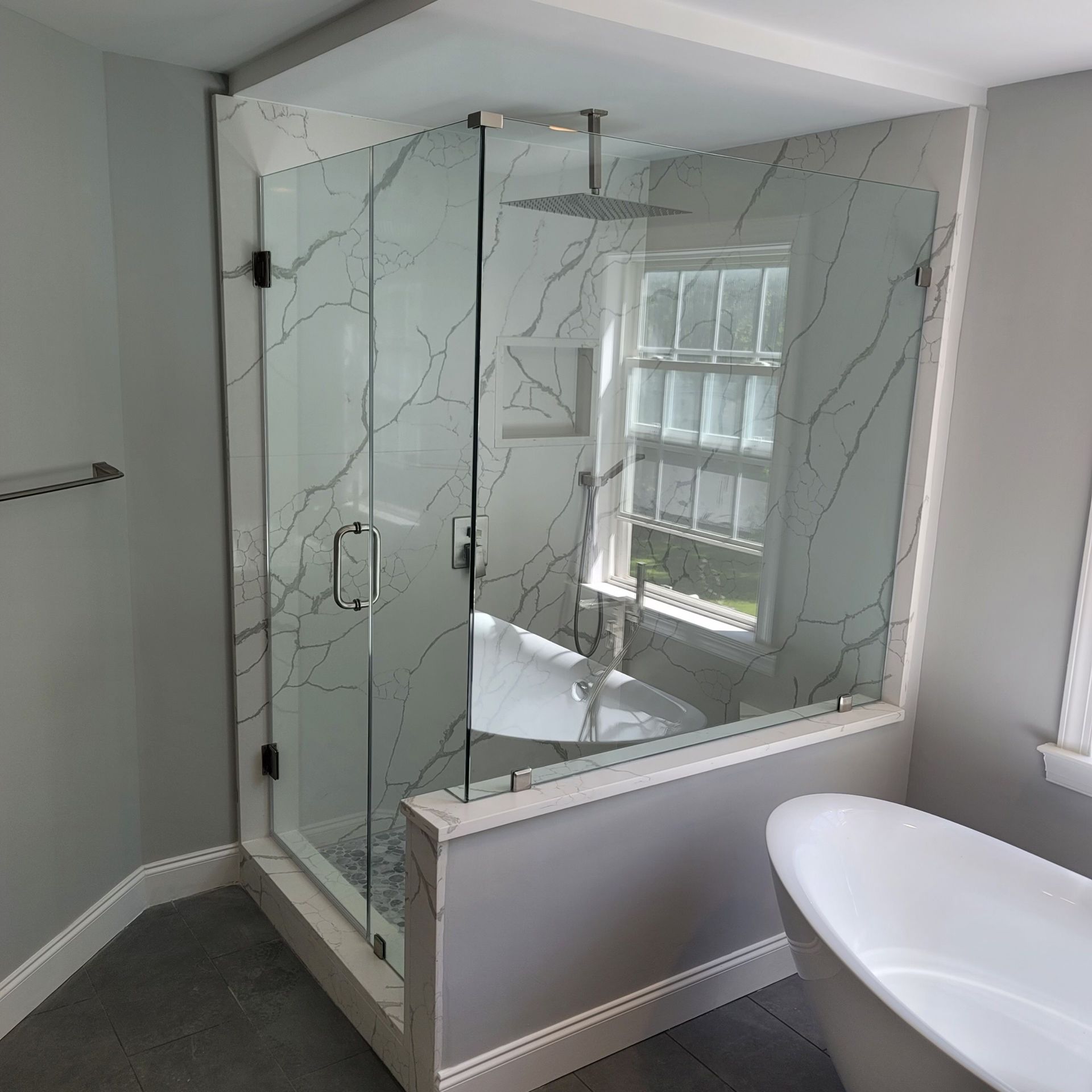 Modern bathroom with a glass shower, marble tile, and a white bathtub.
