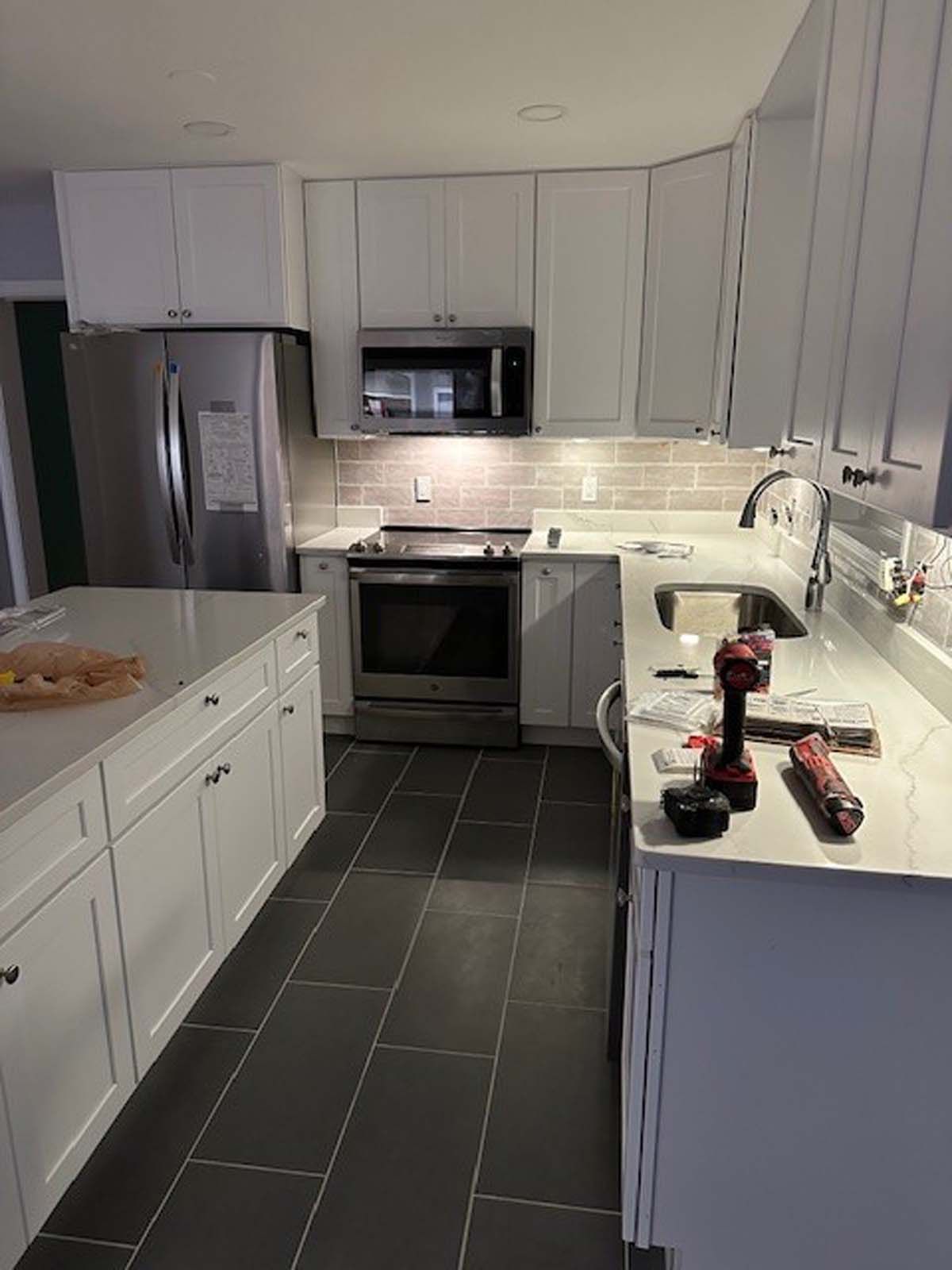 White kitchen with stainless steel appliances, tile backsplash, and dark tile floor.