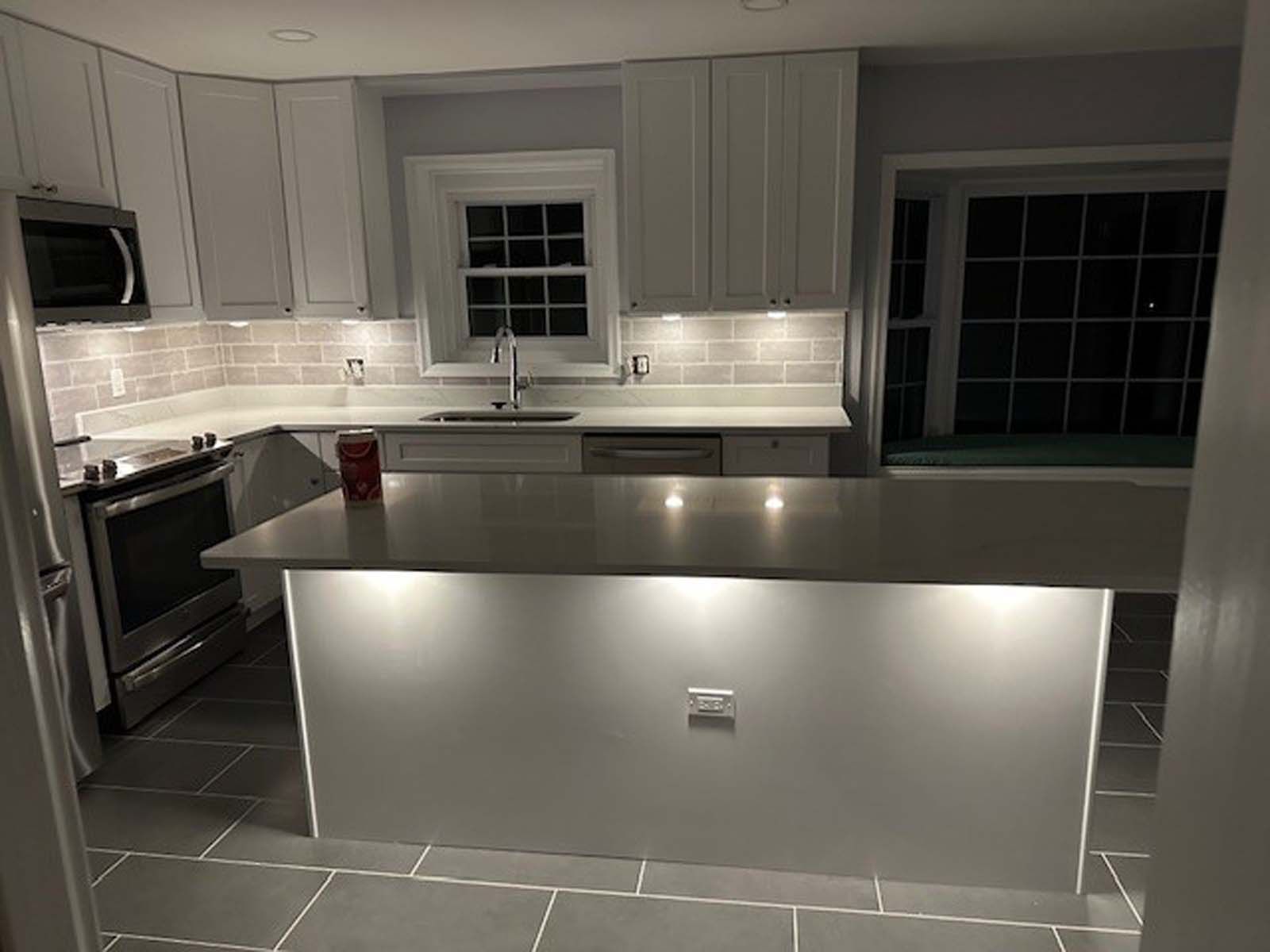 White kitchen with island, stainless steel appliances, gray countertops, and under-cabinet lighting.
