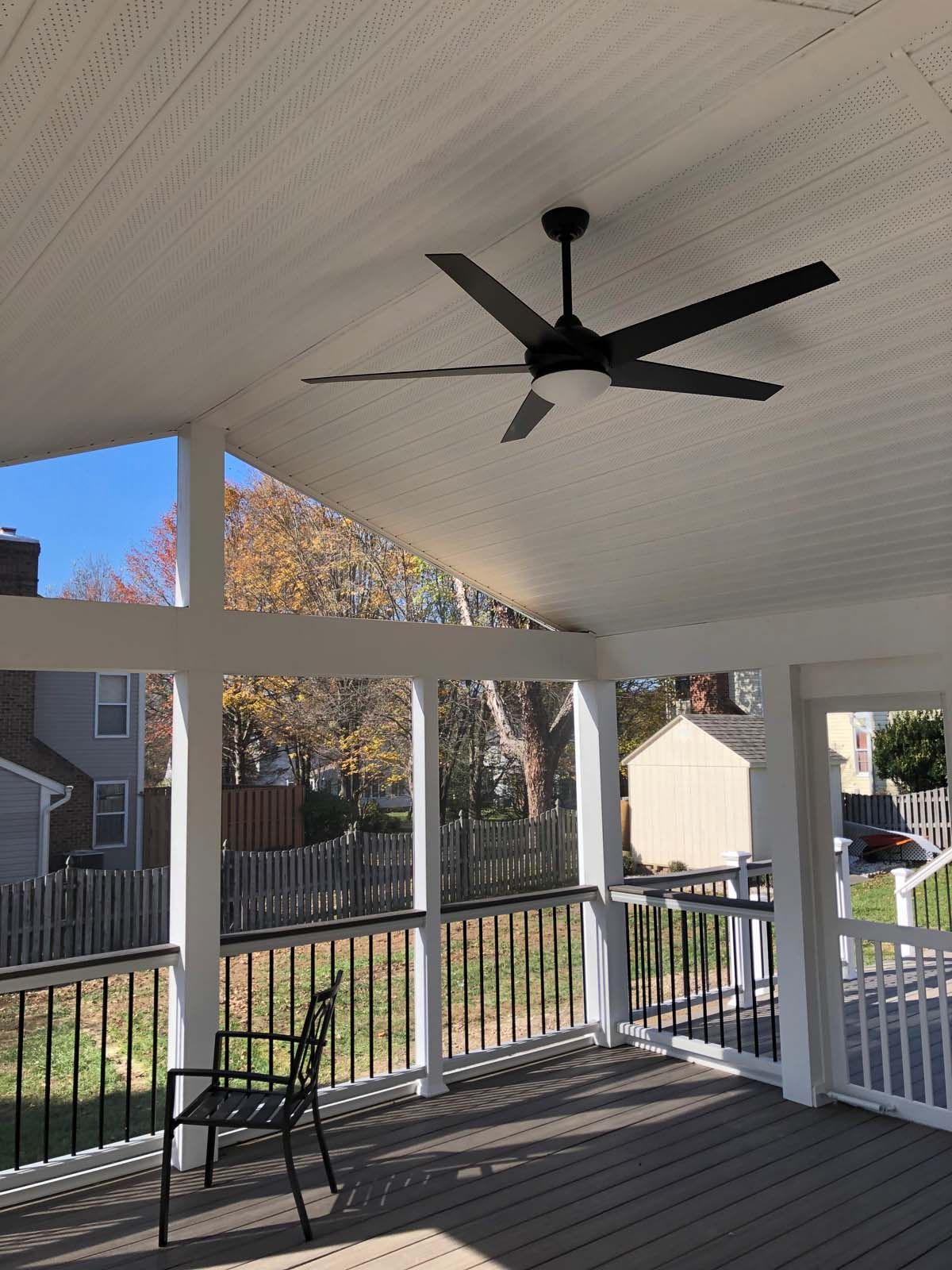 Outdoor covered deck with black ceiling fan, white supports, black railings, and gray deck boards.