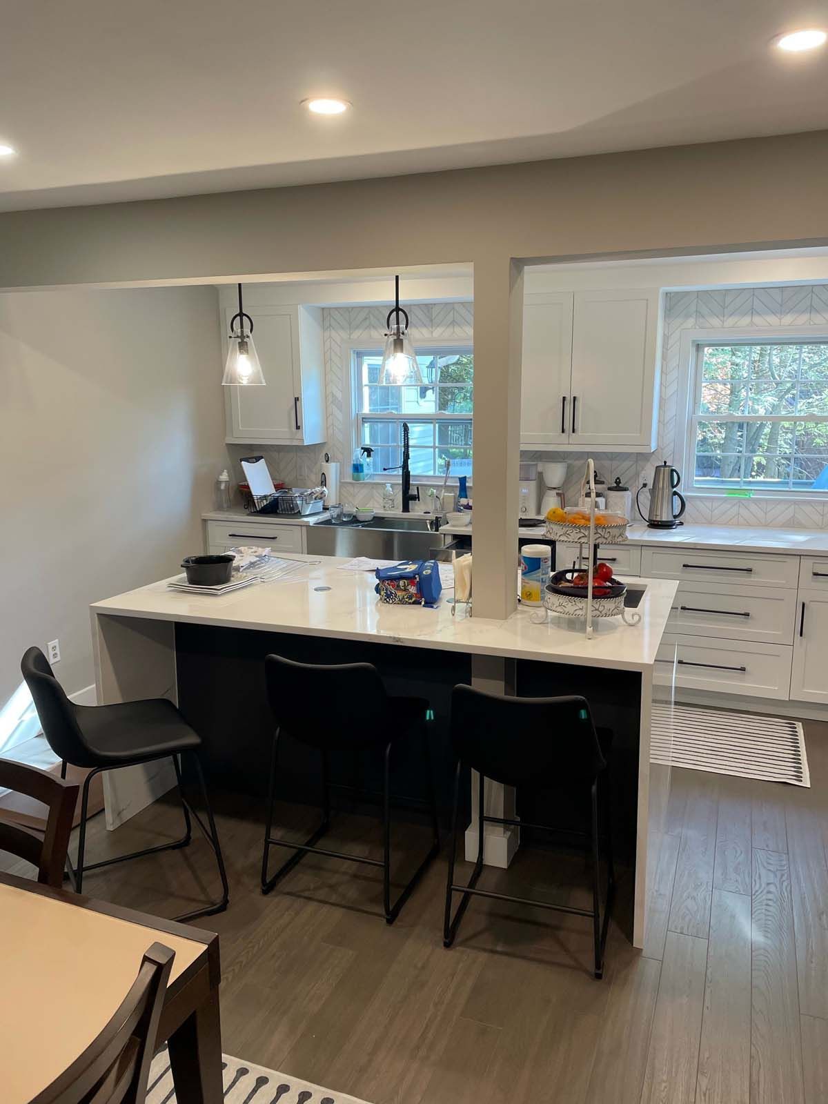 Modern kitchen with an island and bar stools. White cabinets and countertops, dark island.