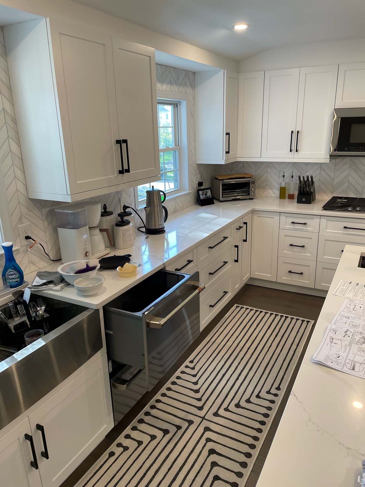 White kitchen with quartz countertops, stainless steel sink, and black hardware.