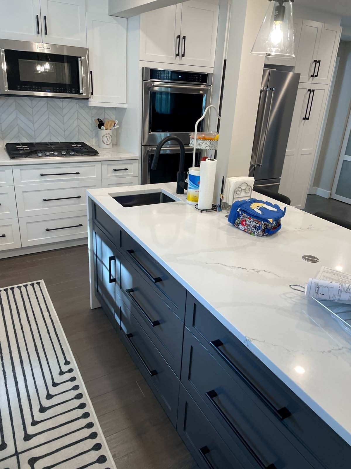 Modern kitchen with white and gray cabinets, island with sink, stainless steel appliances.