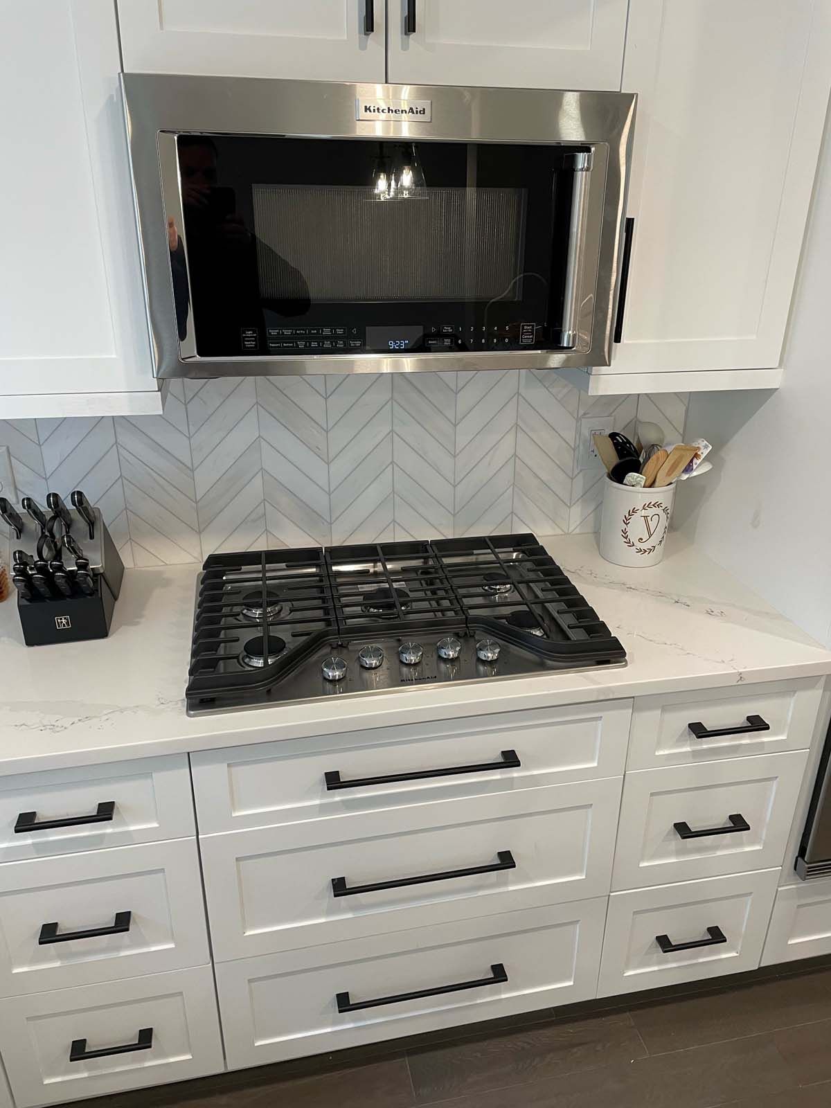 White kitchen with a gas cooktop, microwave, cabinets, and backsplash.