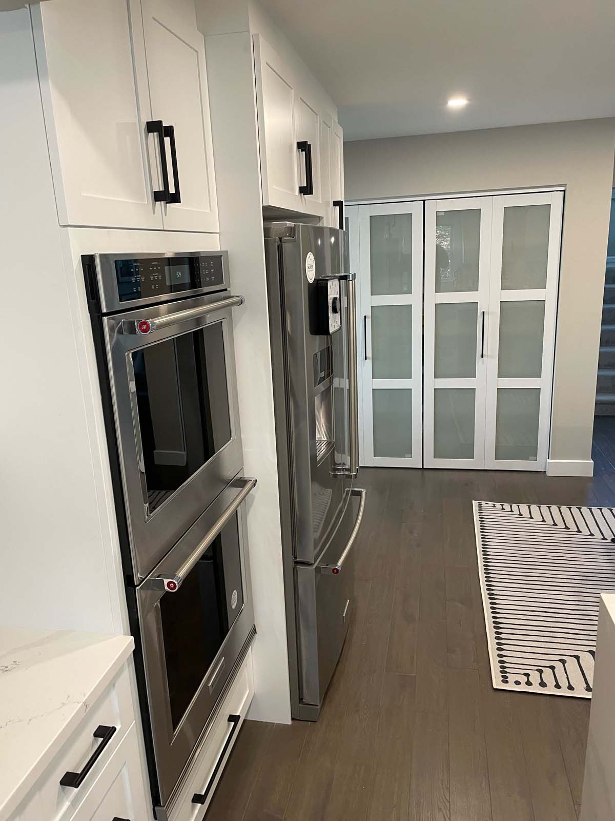 White kitchen cabinets, stainless steel ovens and refrigerator. Frosted glass door.