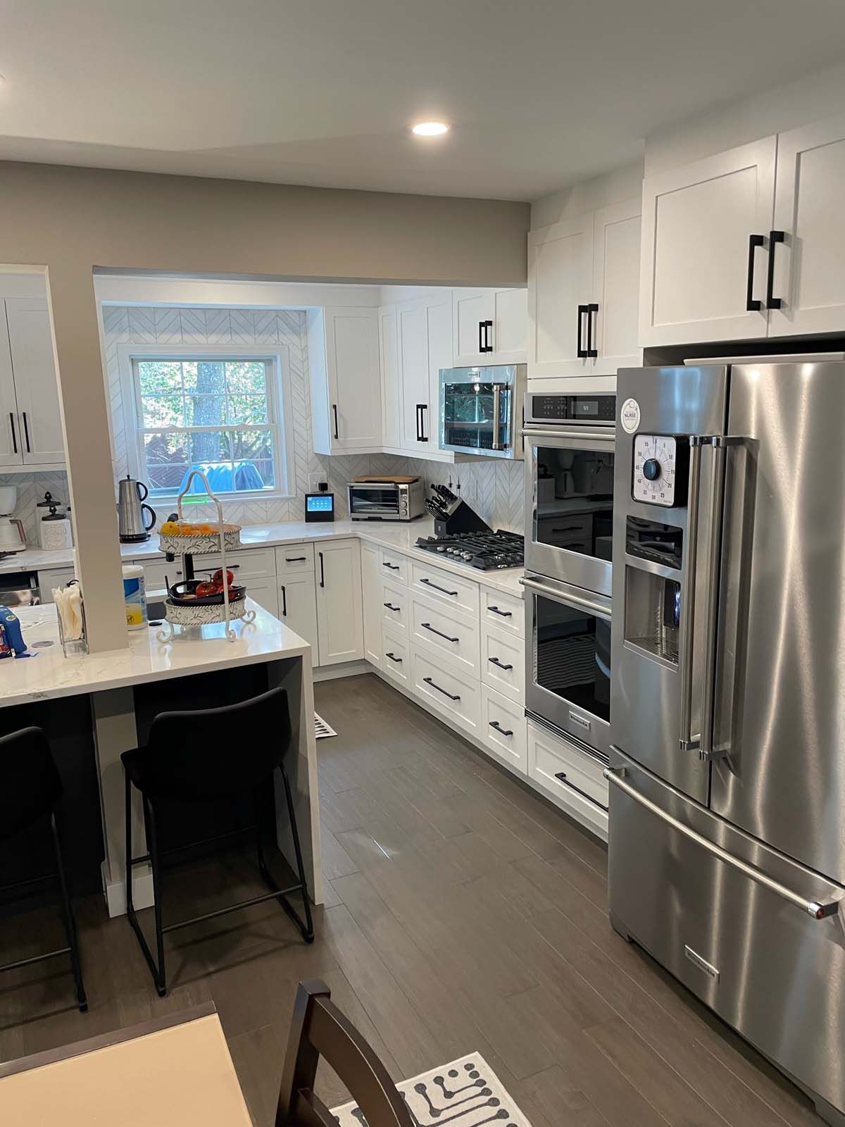 Modern white kitchen with stainless steel appliances, dark cabinets, and wood floor.