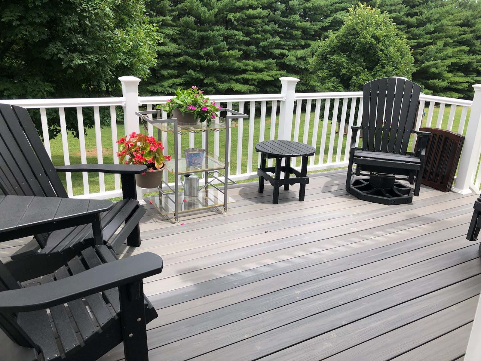 Deck with black Adirondack chairs, potted flowers, and a small table.