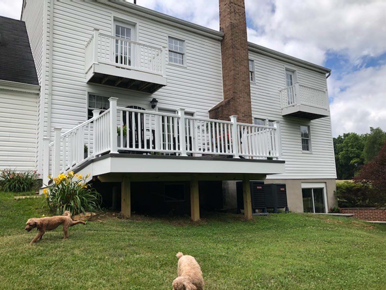 White house with multi-level decks and a chimney, dogs on lawn.