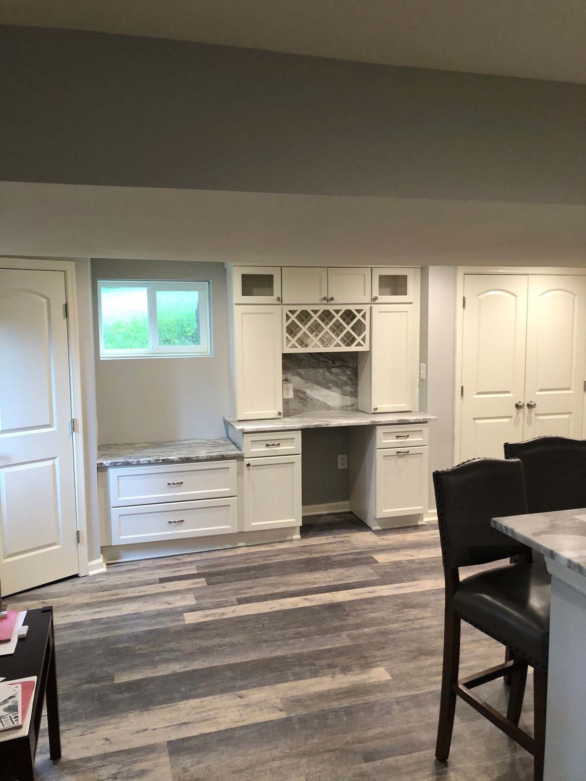A white built-in desk area in a basement with a built-in bench, window, and wine rack.
