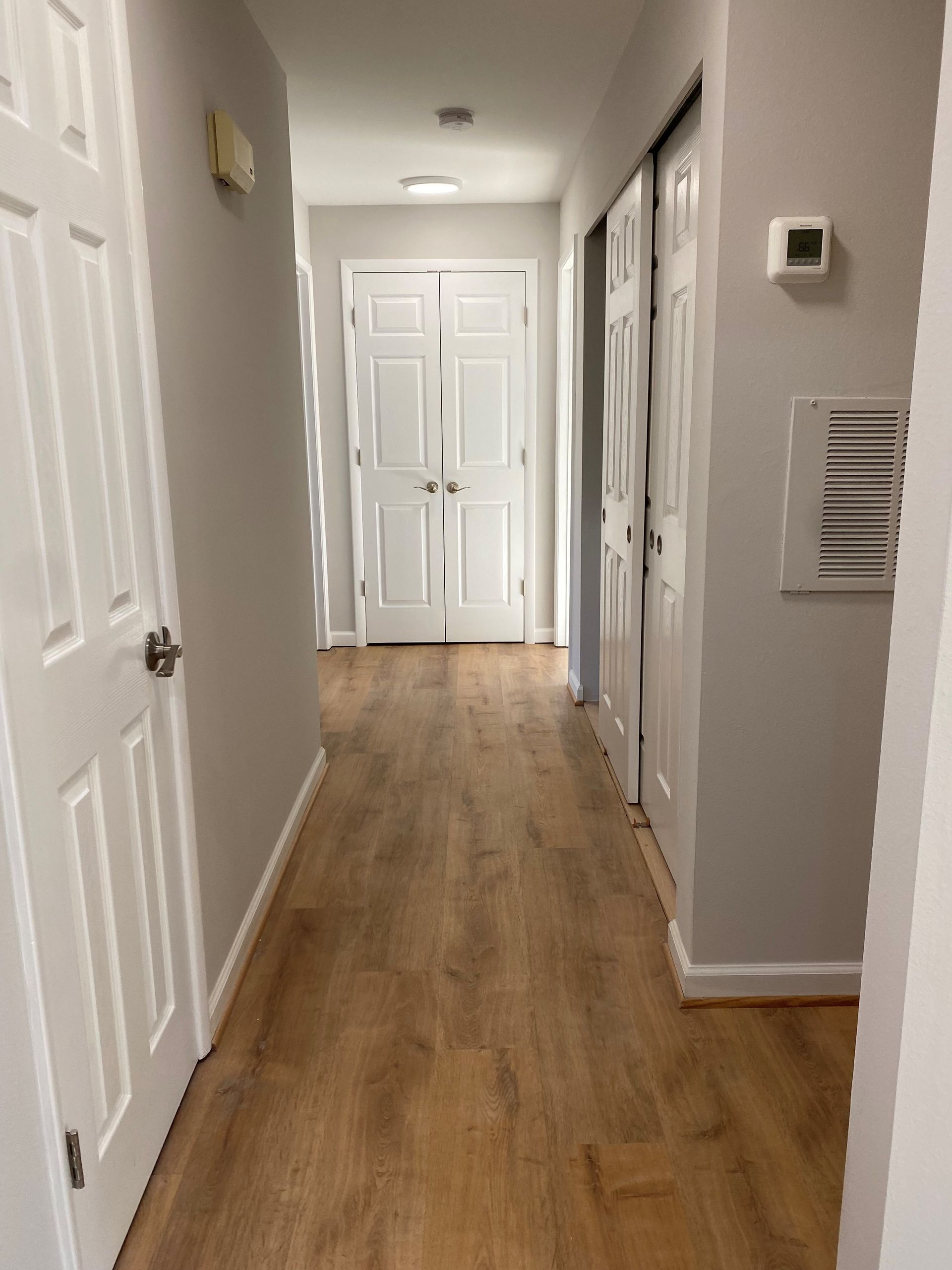 Hallway with wood-look floor, gray walls, white doors and trim, and a closet with sliding doors.