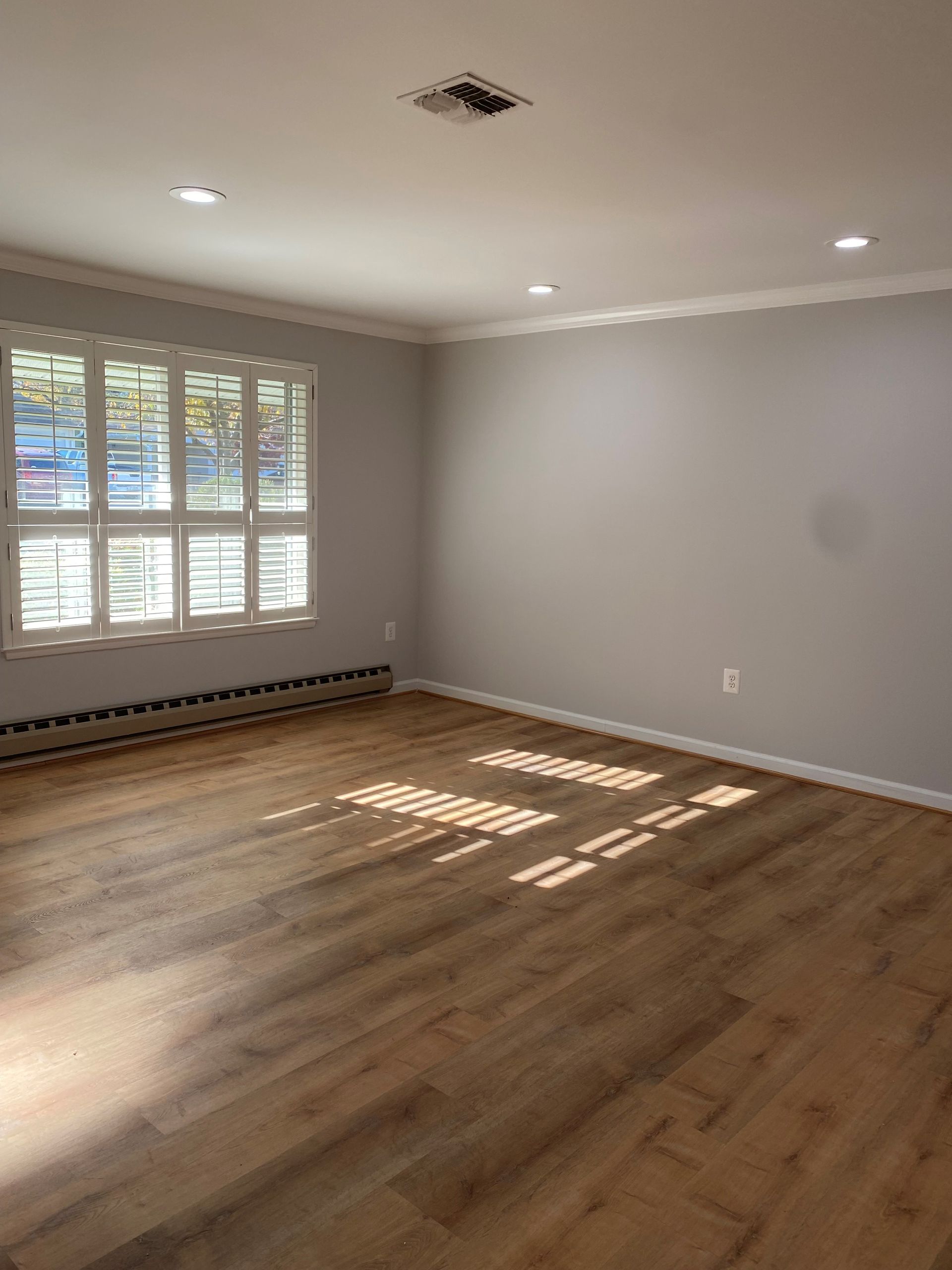 Empty room with hardwood floors, gray walls, white trim and a window.