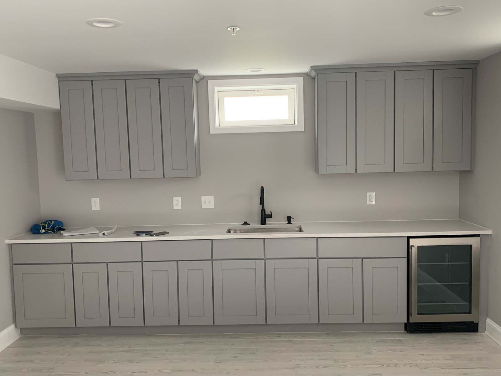 Gray kitchen cabinets with a sink and small refrigerator in a room.