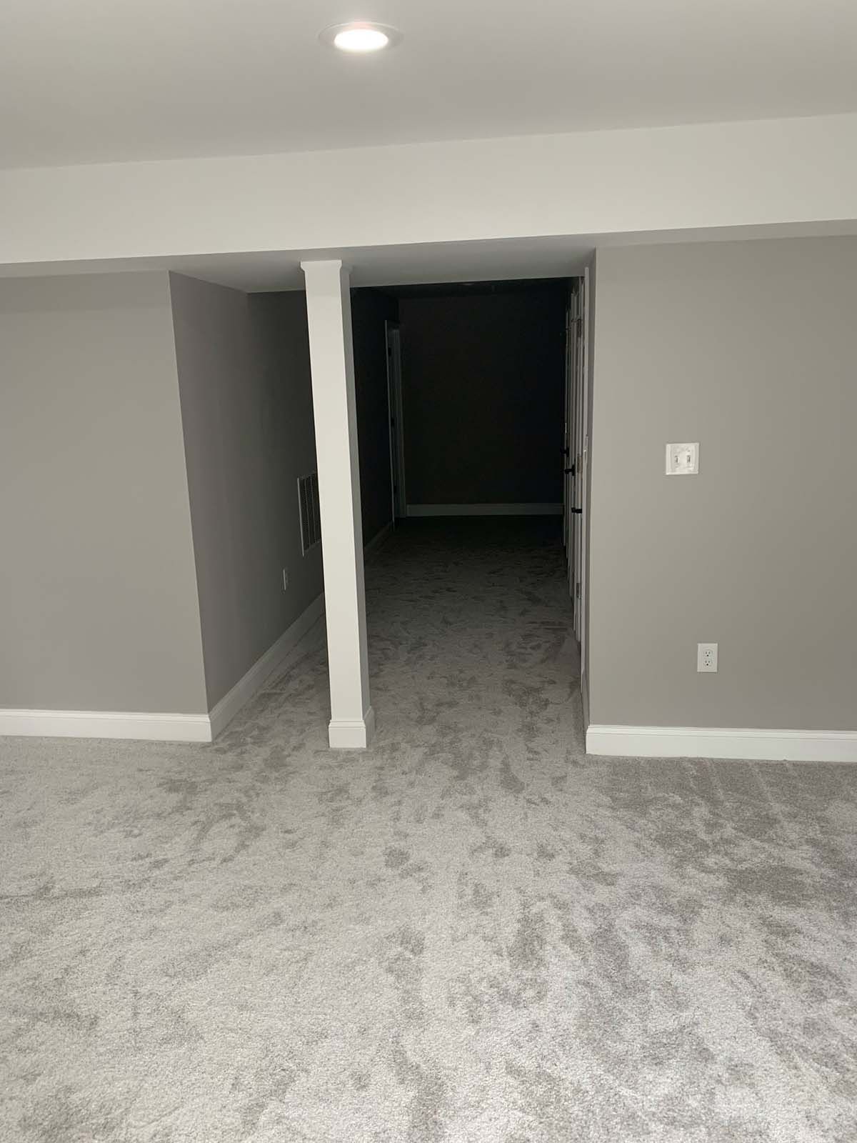 Grey carpeted room with a doorway leading to a dark hallway, white trim, and gray walls.