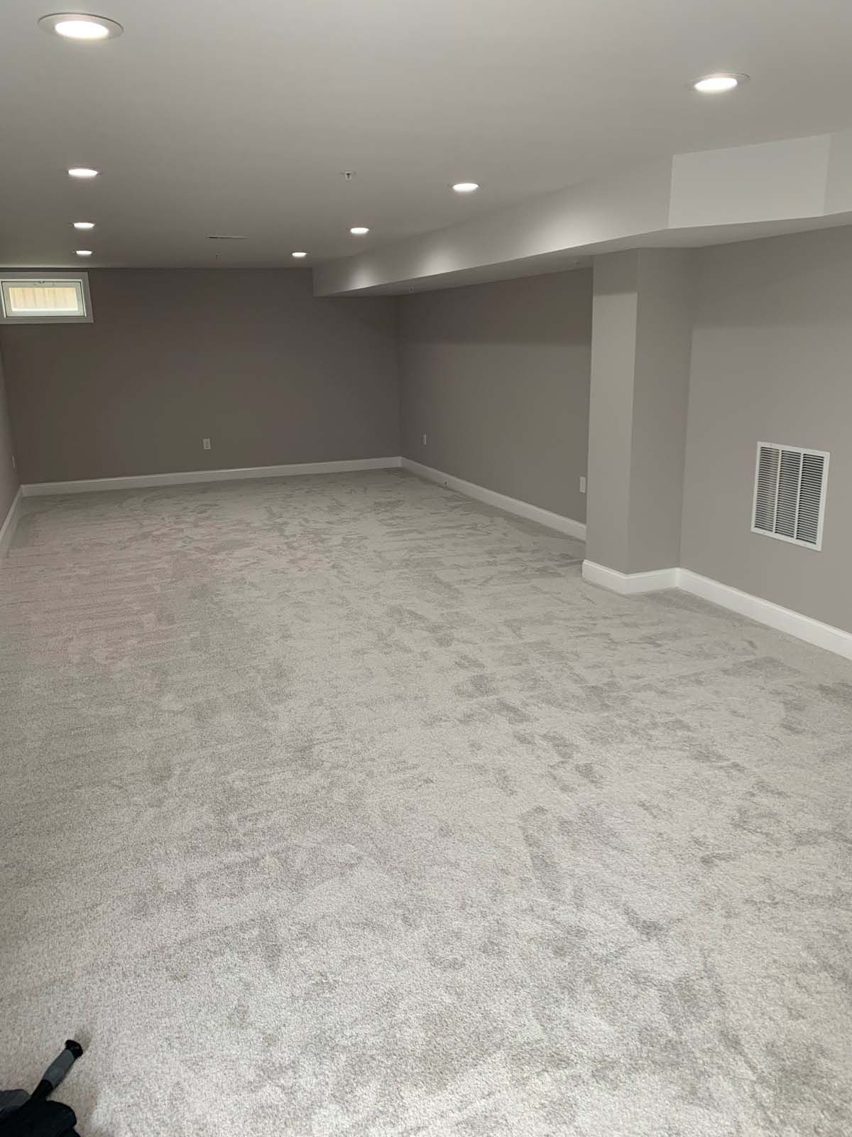 Empty, light-filled basement with gray carpet, light gray walls, recessed lighting, and a small window.