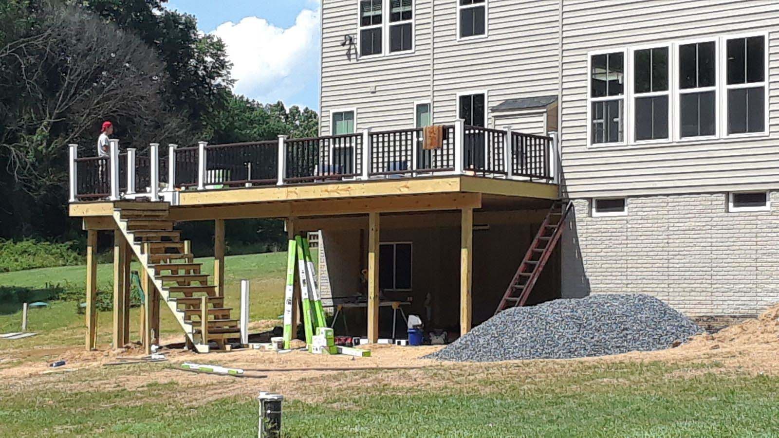 A two-story house with a partially built wooden deck and stairs on a grassy area.