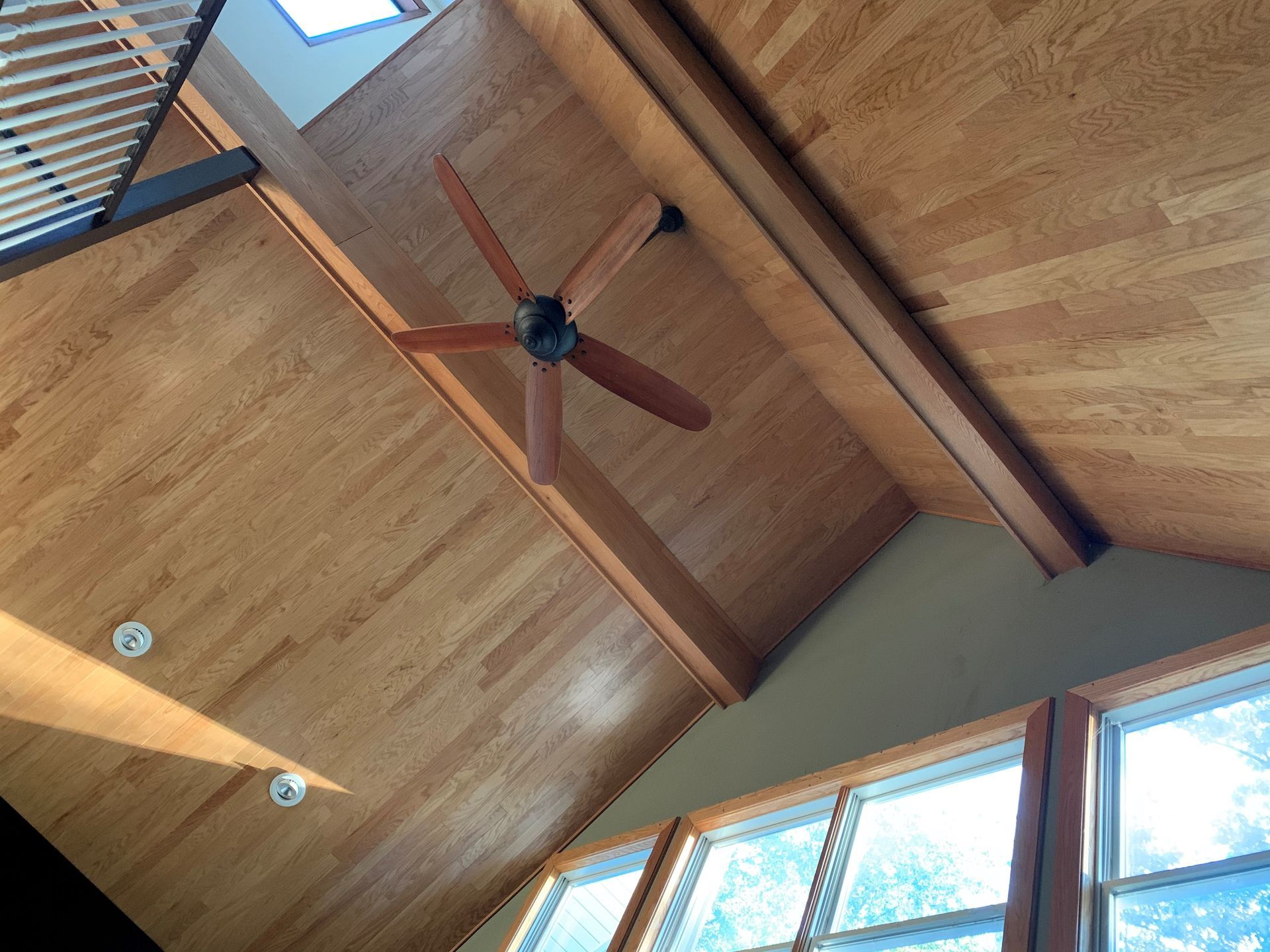 Wooden vaulted ceiling with a ceiling fan and windows.