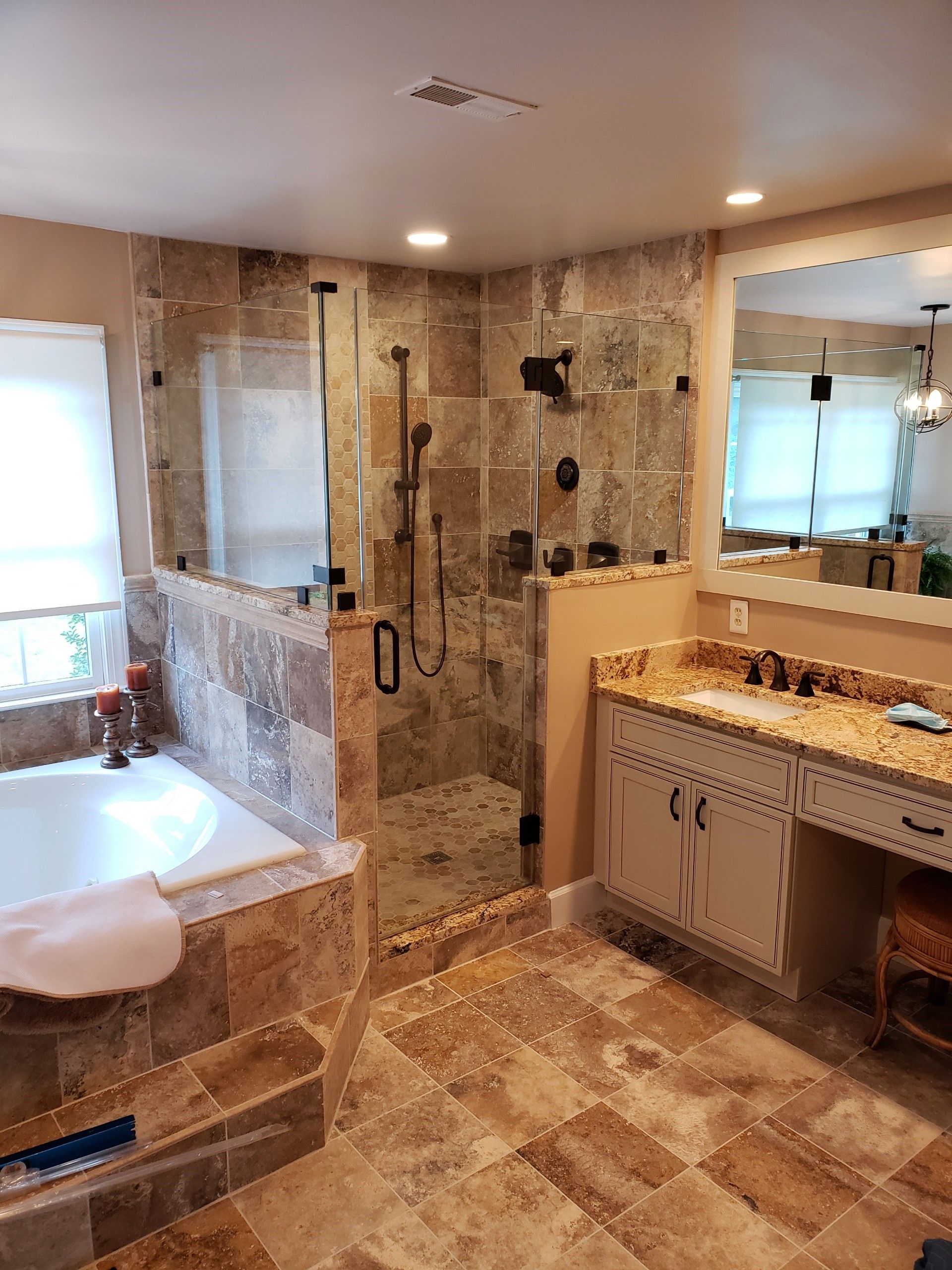 Spacious bathroom with a glass shower, a bathtub, vanity, and stone tile floors.