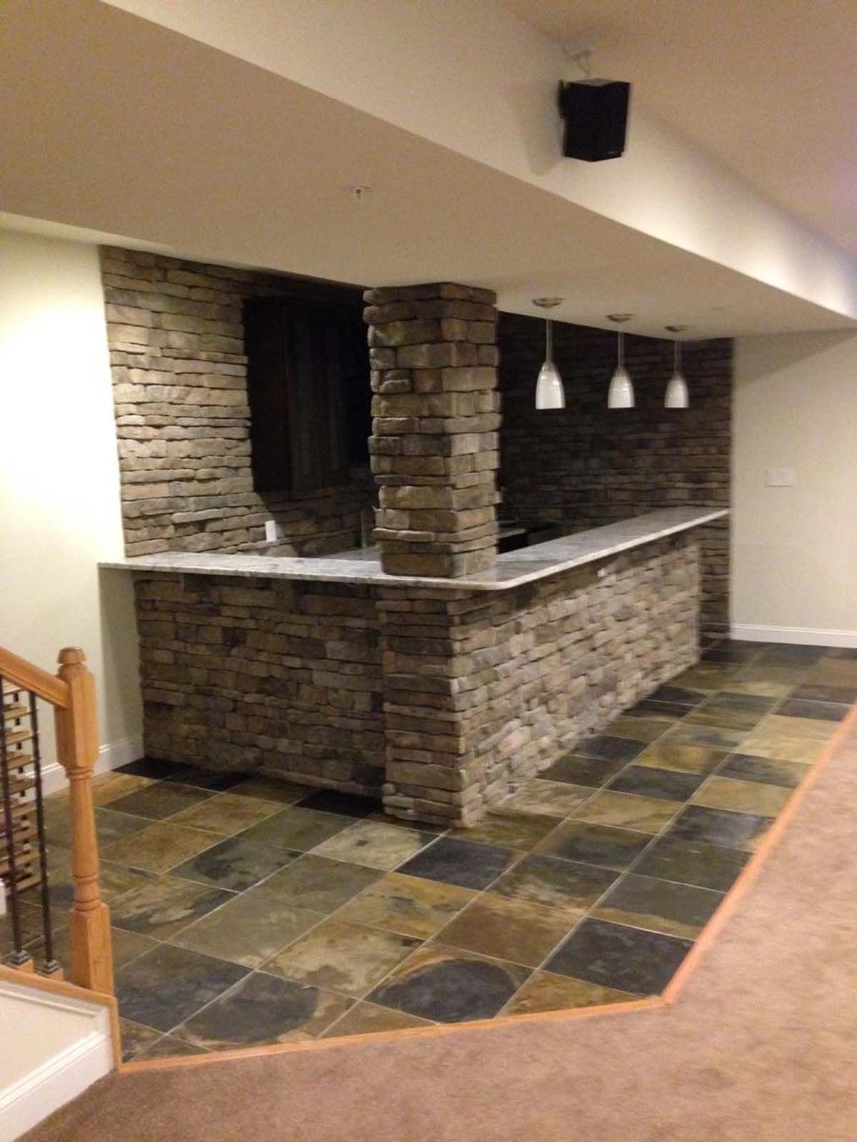 Basement bar with stone facade, white counter, pendant lights, and patterned floor tiles.