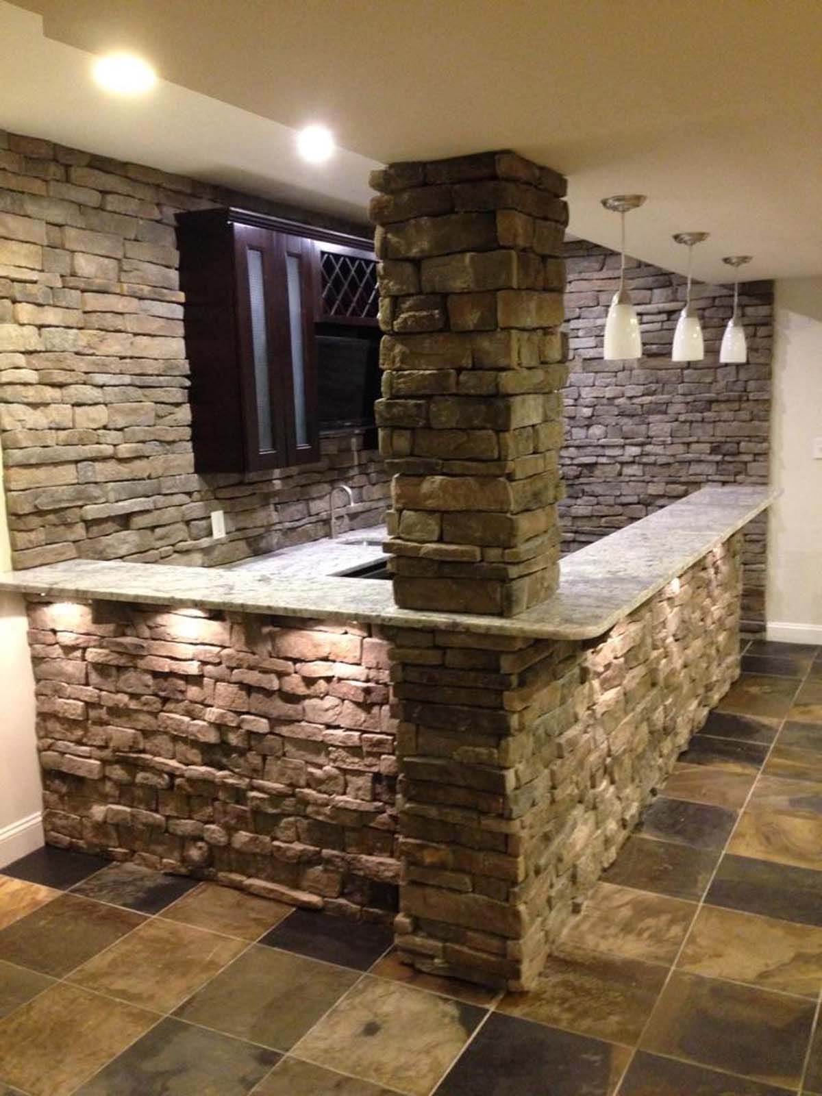 Stone-faced bar with granite countertop and overhead lighting in a finished basement.