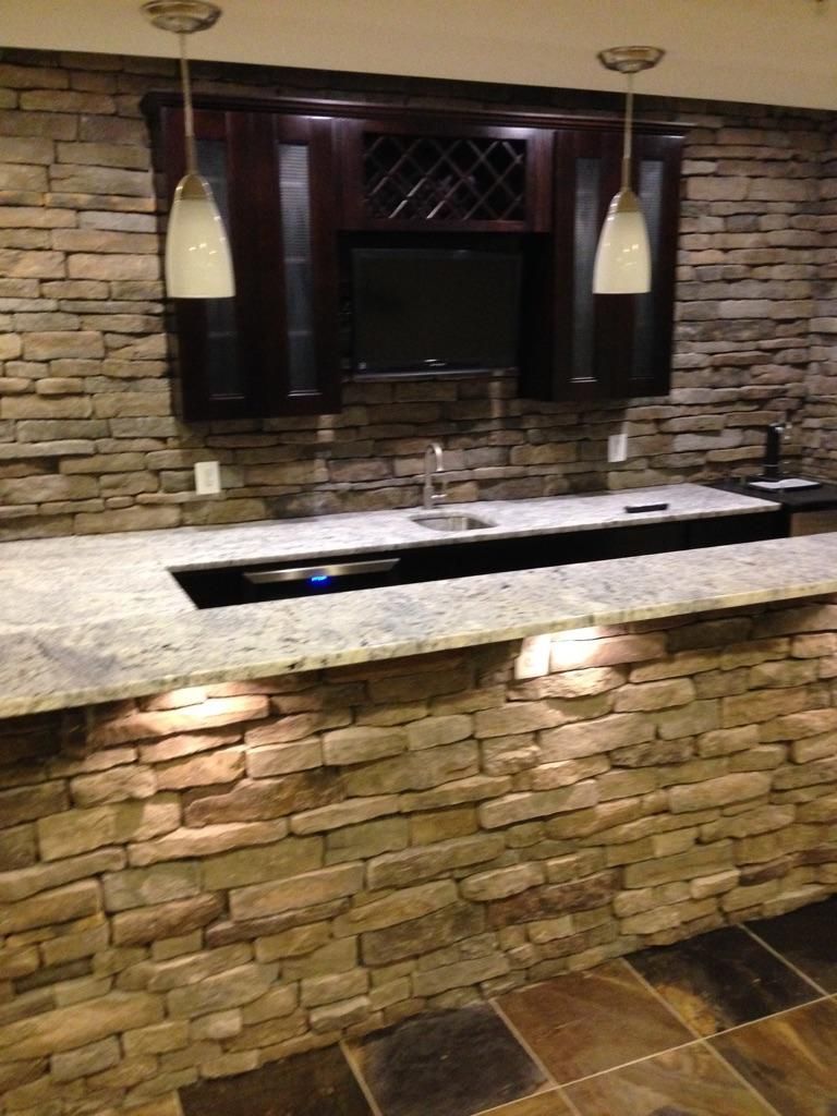 Bar with stone facing, granite countertop, and built-in sink, with dark cabinets and two pendant lights.