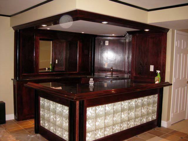 Dark wood home bar with glass block facade, sink, and overhead cabinets.