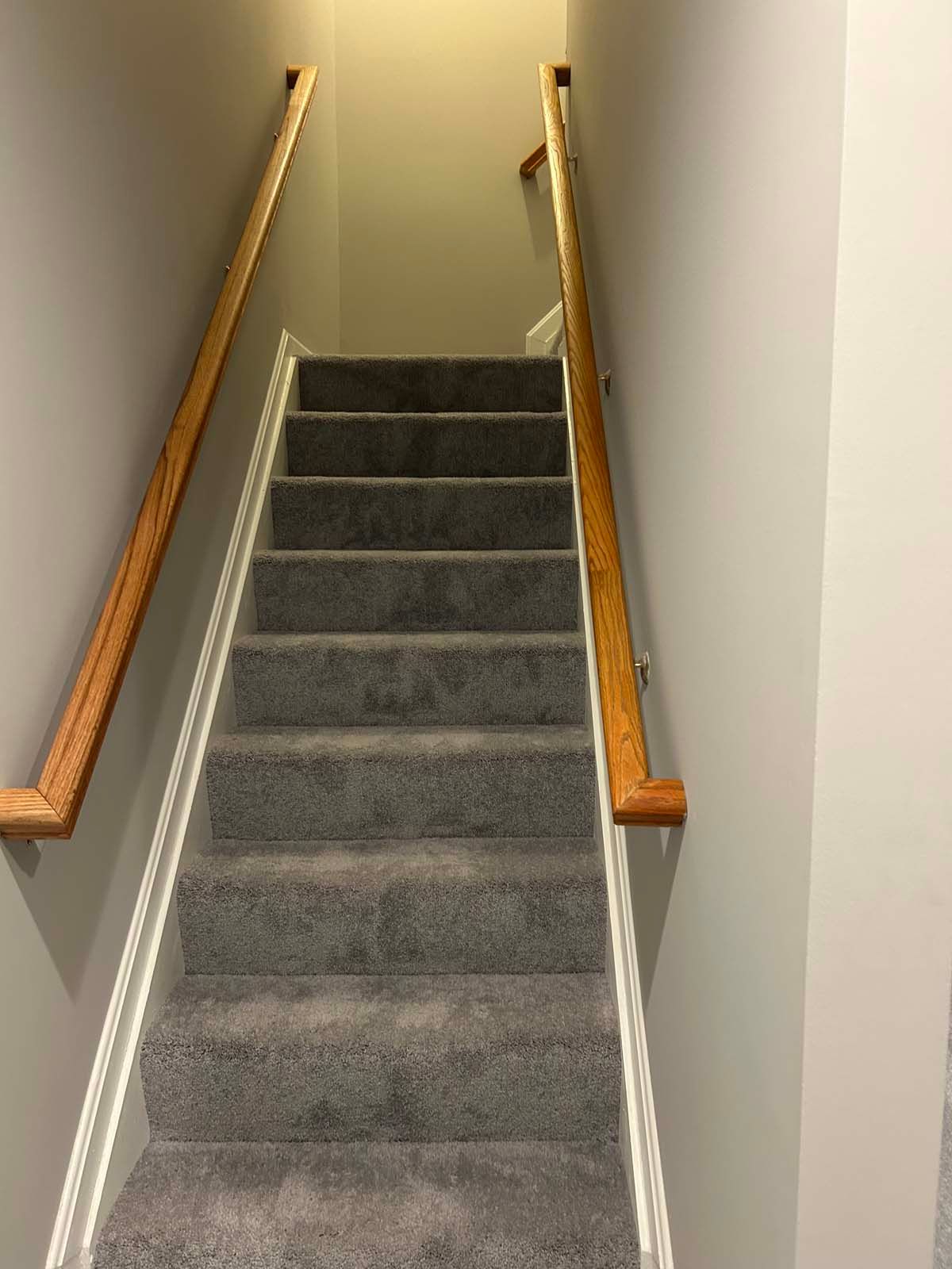 Staircase with gray carpet and wooden handrails, ascending between gray walls.