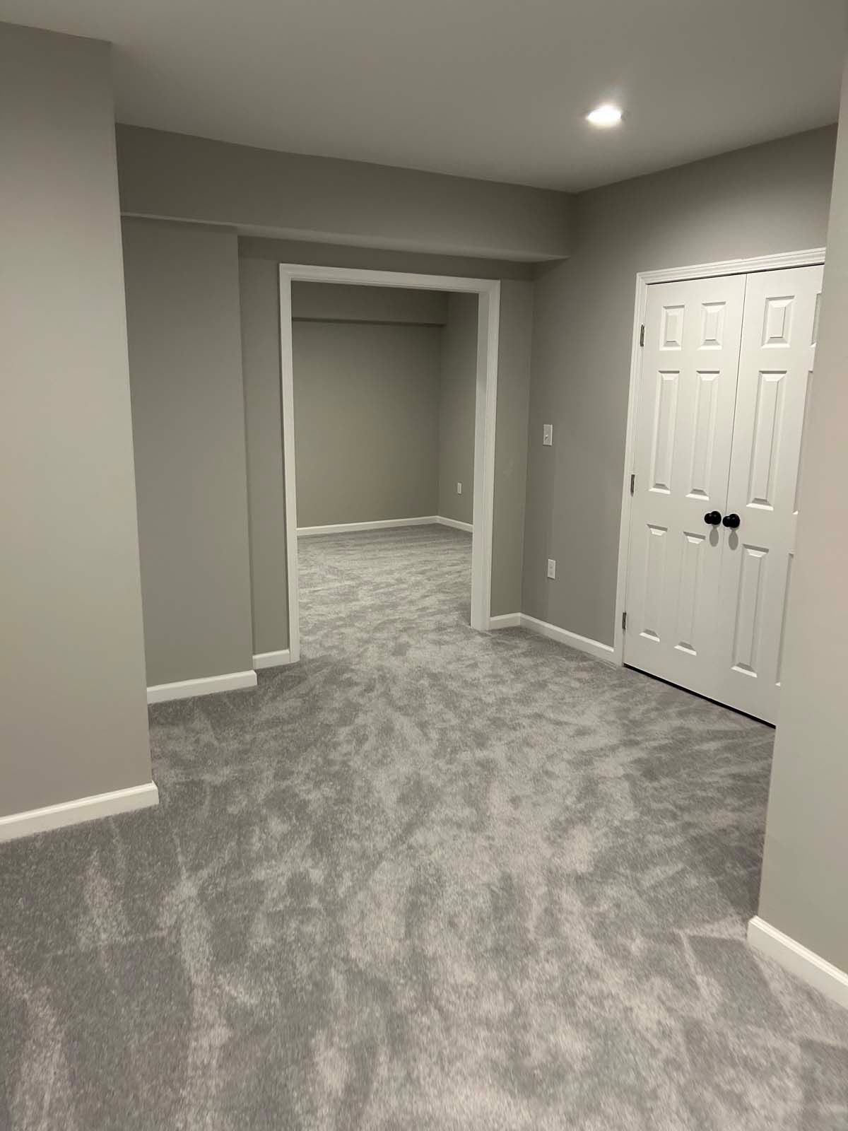 A gray carpeted room with a doorway, a white door, and gray walls.