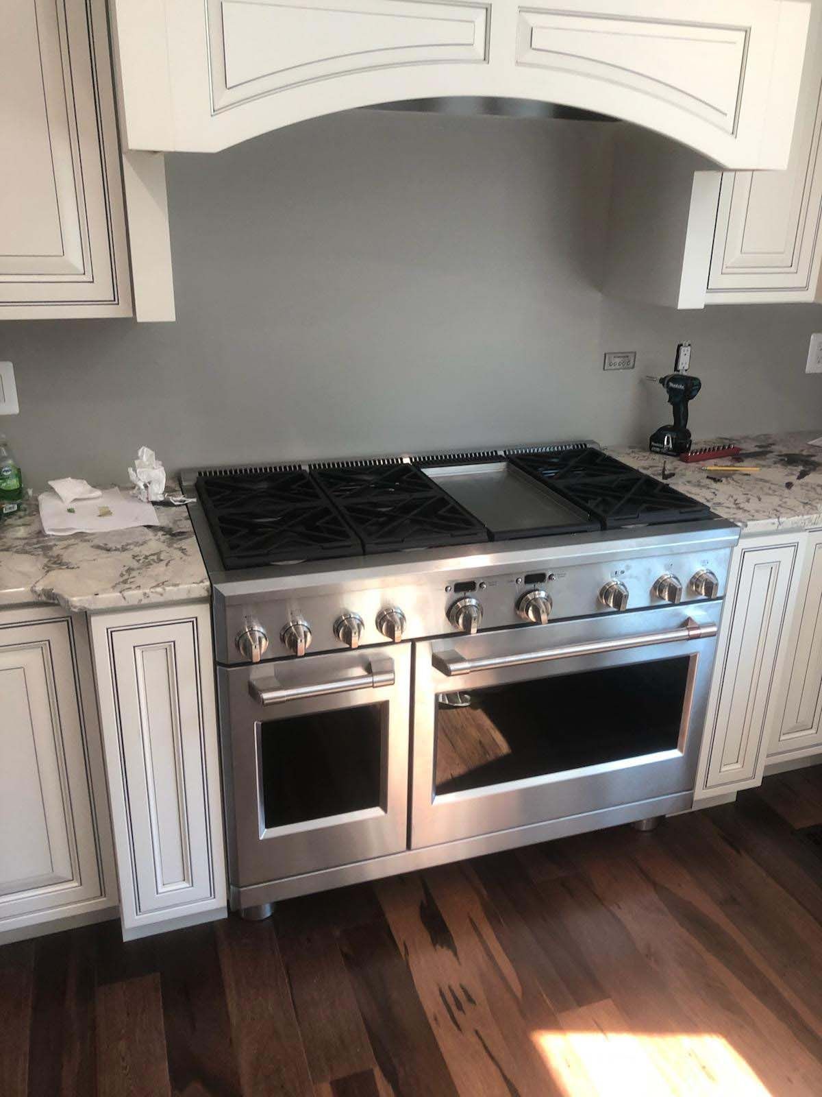 Stainless steel range and hood in a kitchen with white cabinets and wooden floors.