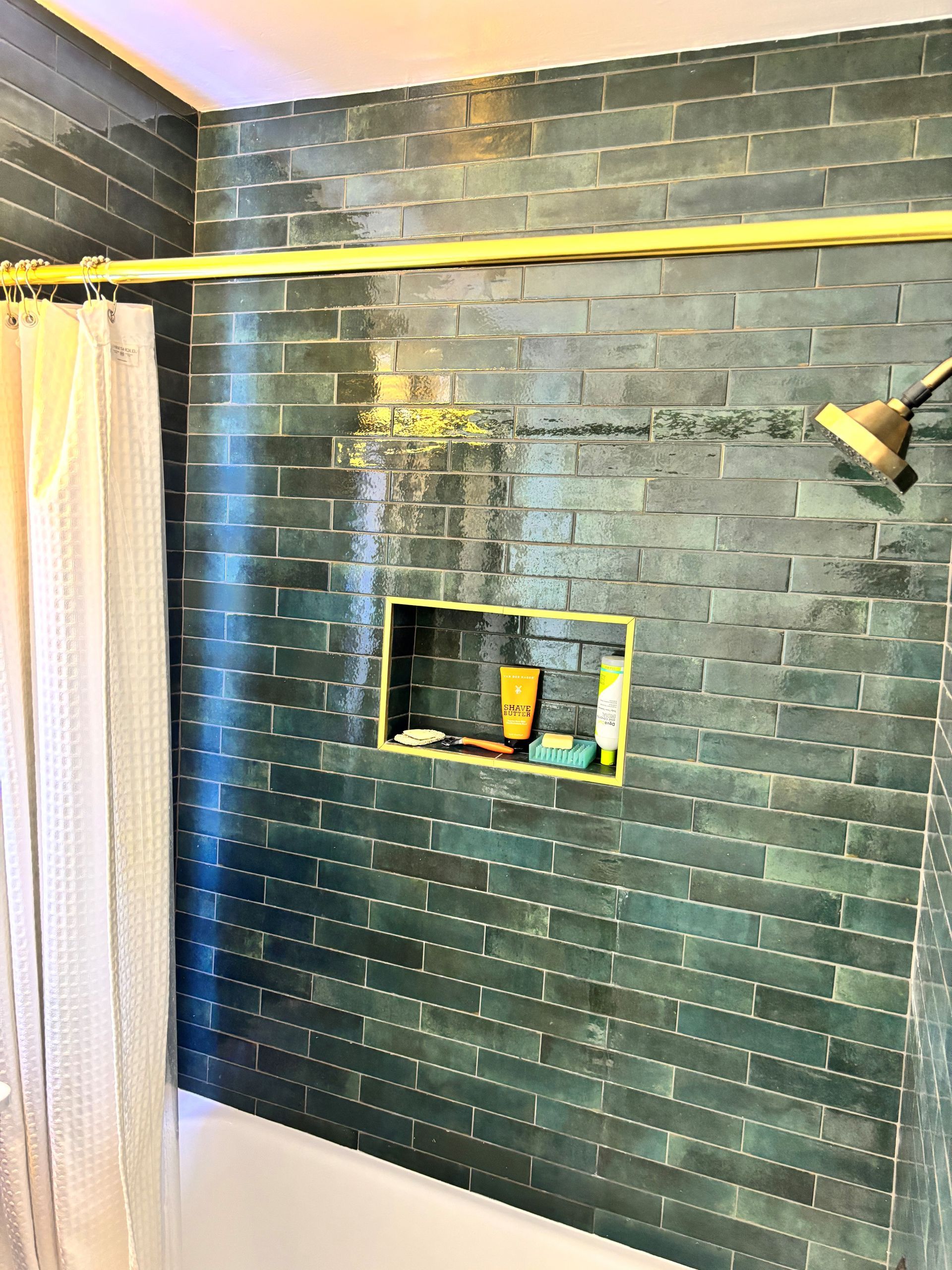 Dark teal-tiled shower with built-in shelf, a yellow curtain rod, and a showerhead.