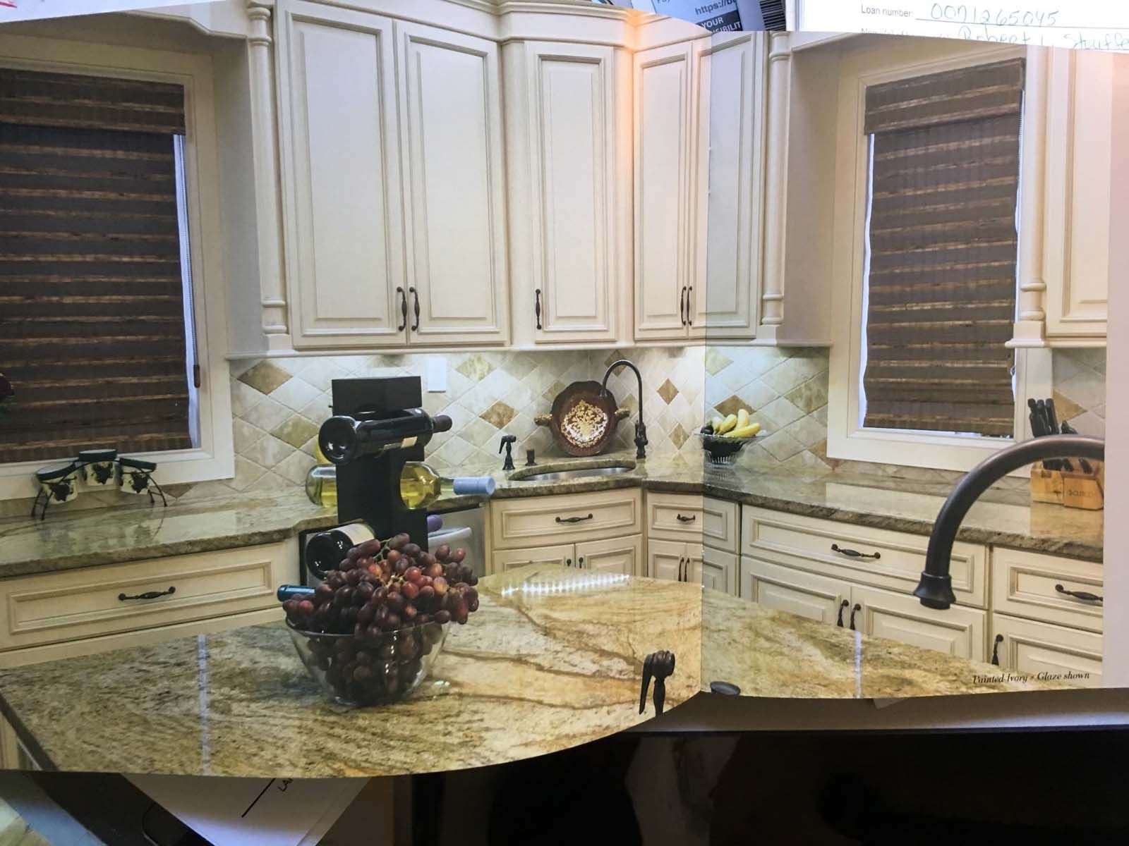 Cream kitchen cabinets with granite countertops, brown blinds, and fruit bowl.