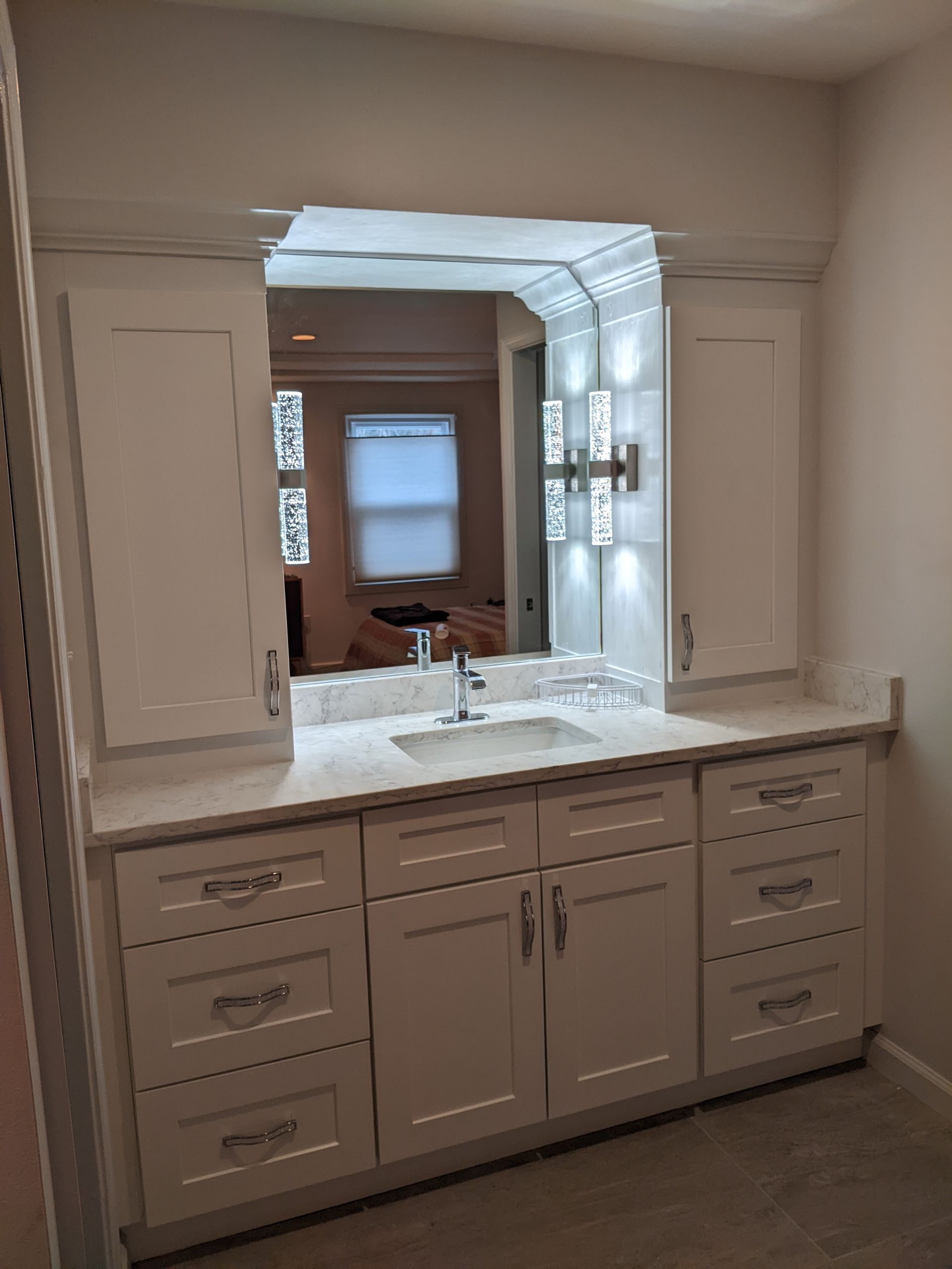 White vanity with sink and mirror, flanked by cabinets, in a bathroom. Recessed lighting.