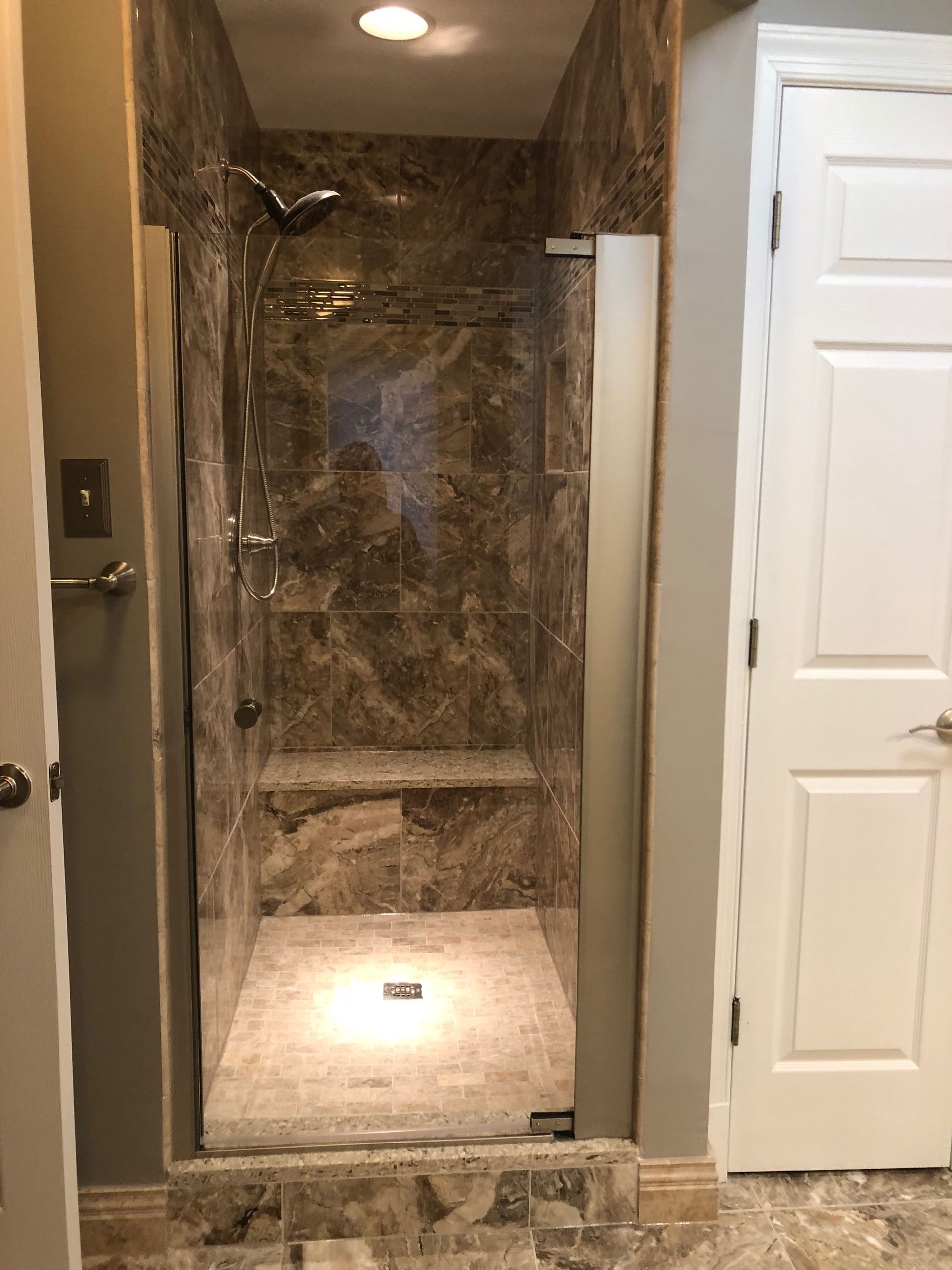 Walk-in shower with marble-like tile, glass door, and a built-in bench.