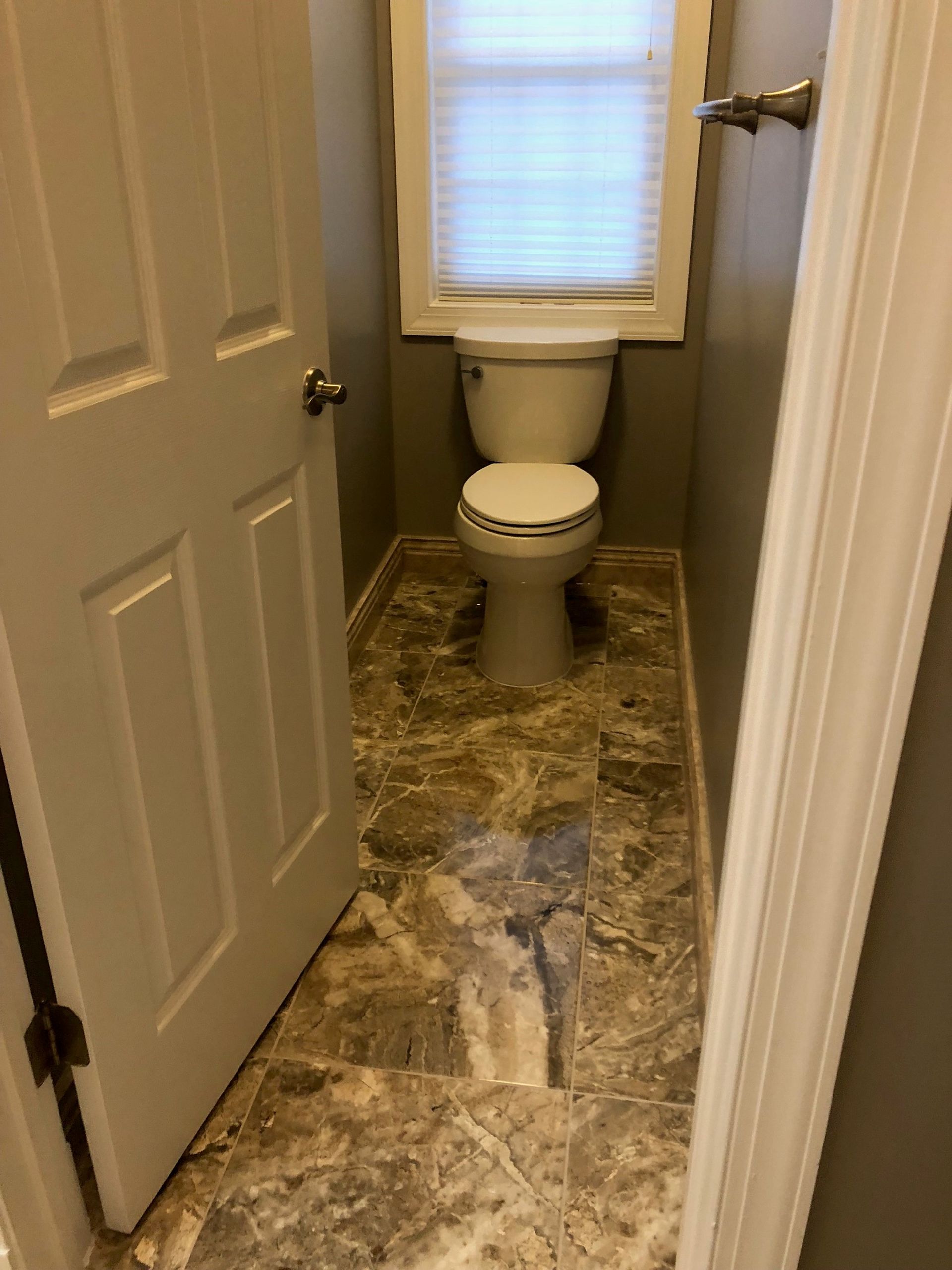 Bathroom with toilet, patterned floor, and a window with blinds.