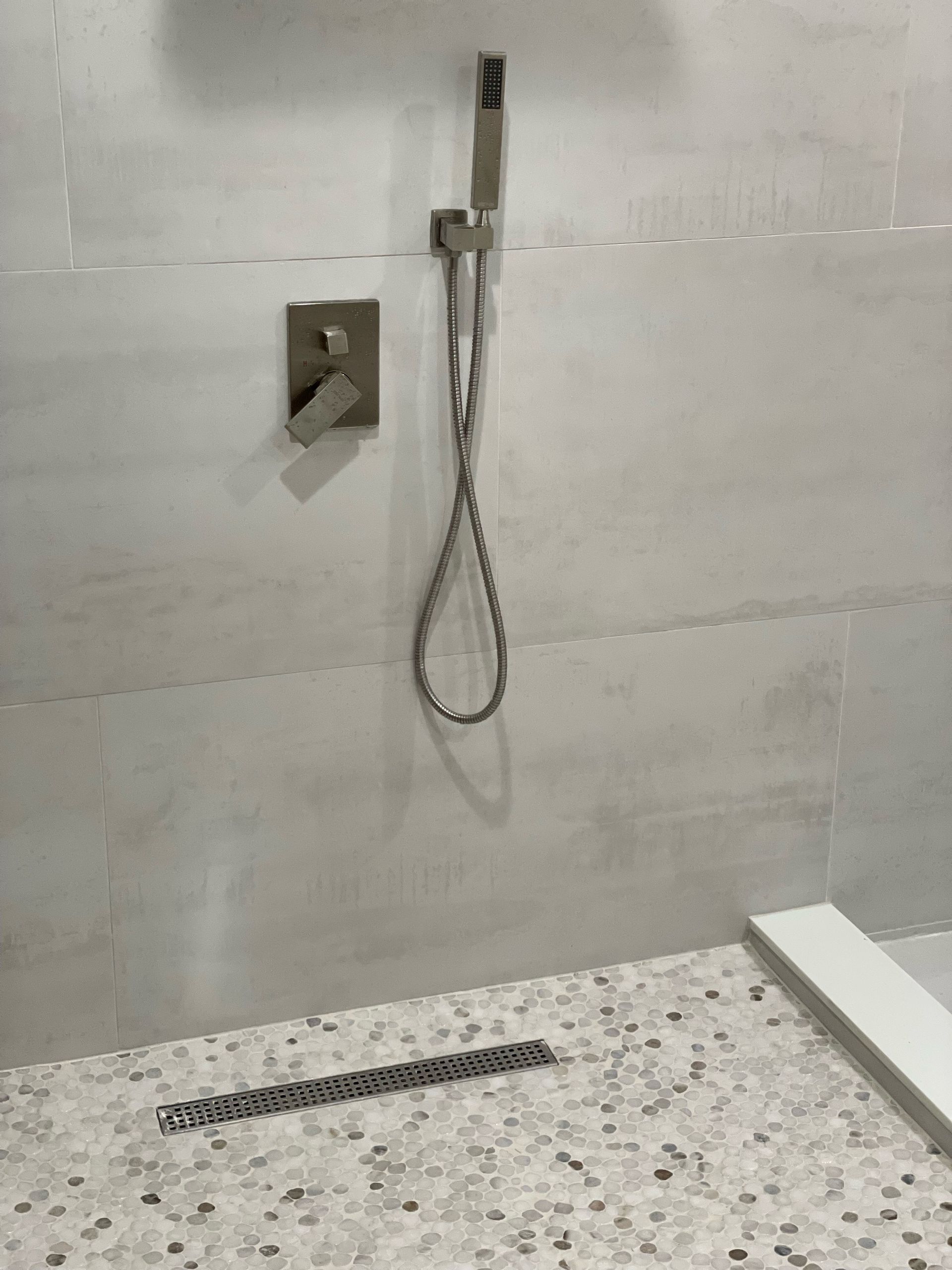 Shower with white tile, hand shower, and mosaic tile floor.